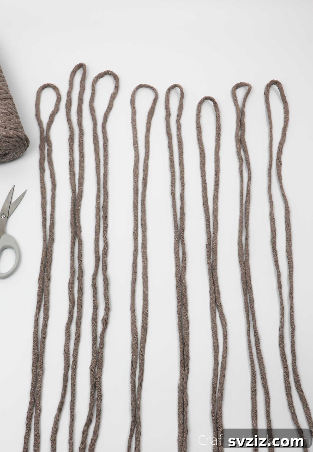 Eight neatly arranged sixty-inch pieces of cappuccino-colored yarn, cut and ready for use.