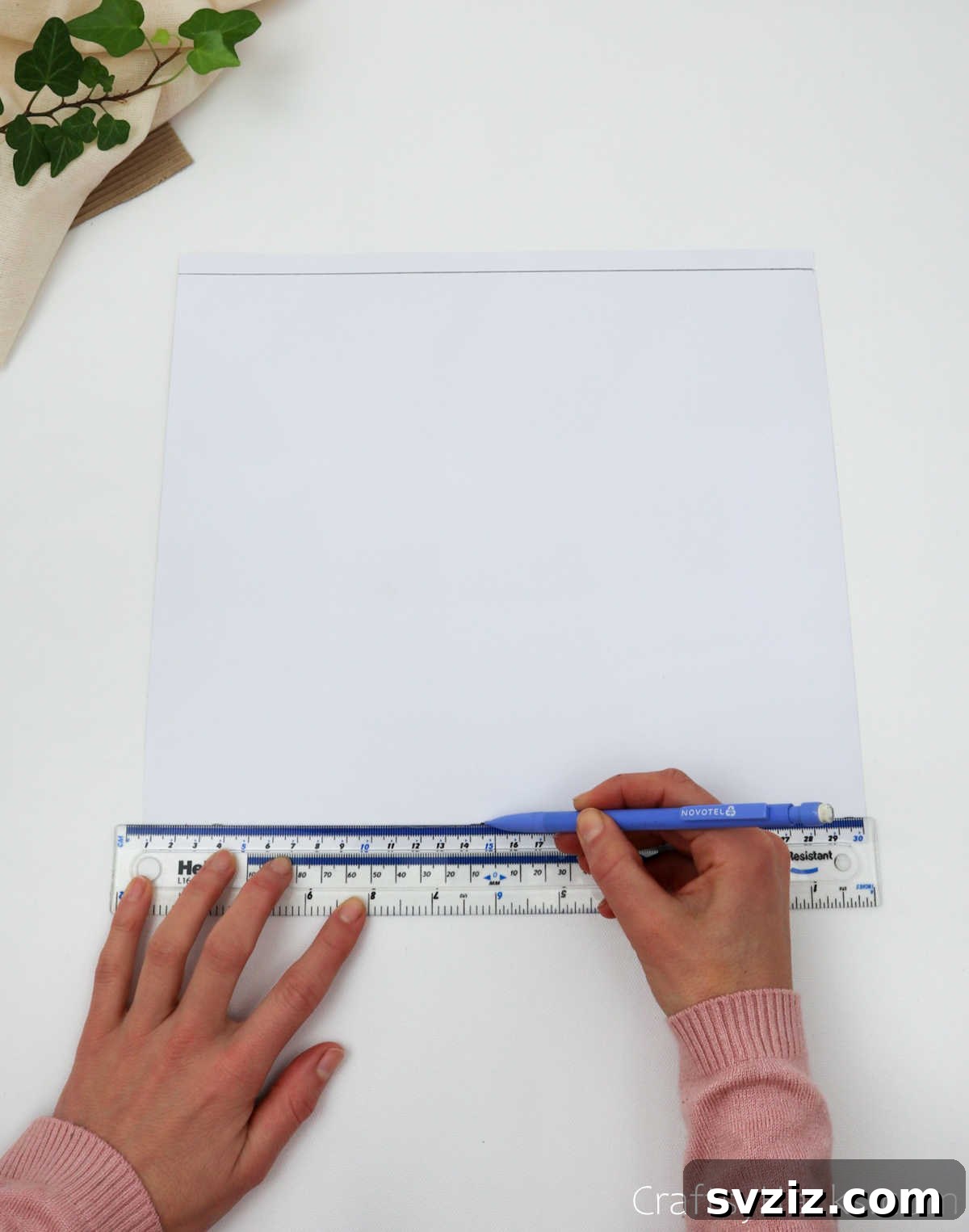 Craft Your Own Stunning Paper Lanterns 6 A ruler and pencil are used to trace a horizontal guide line across the craft paper, preparing it for cuts.