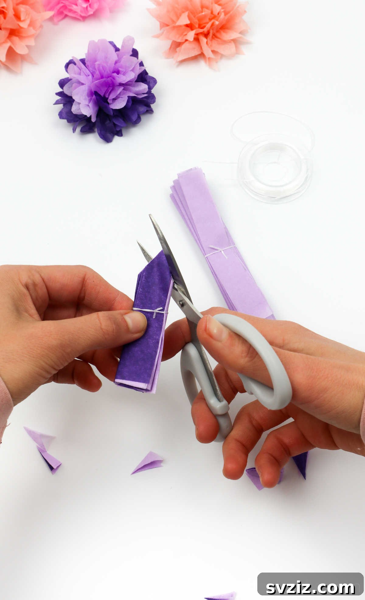 A person using scissors to cut the edges of a folded tissue paper bundle into a decorative shape