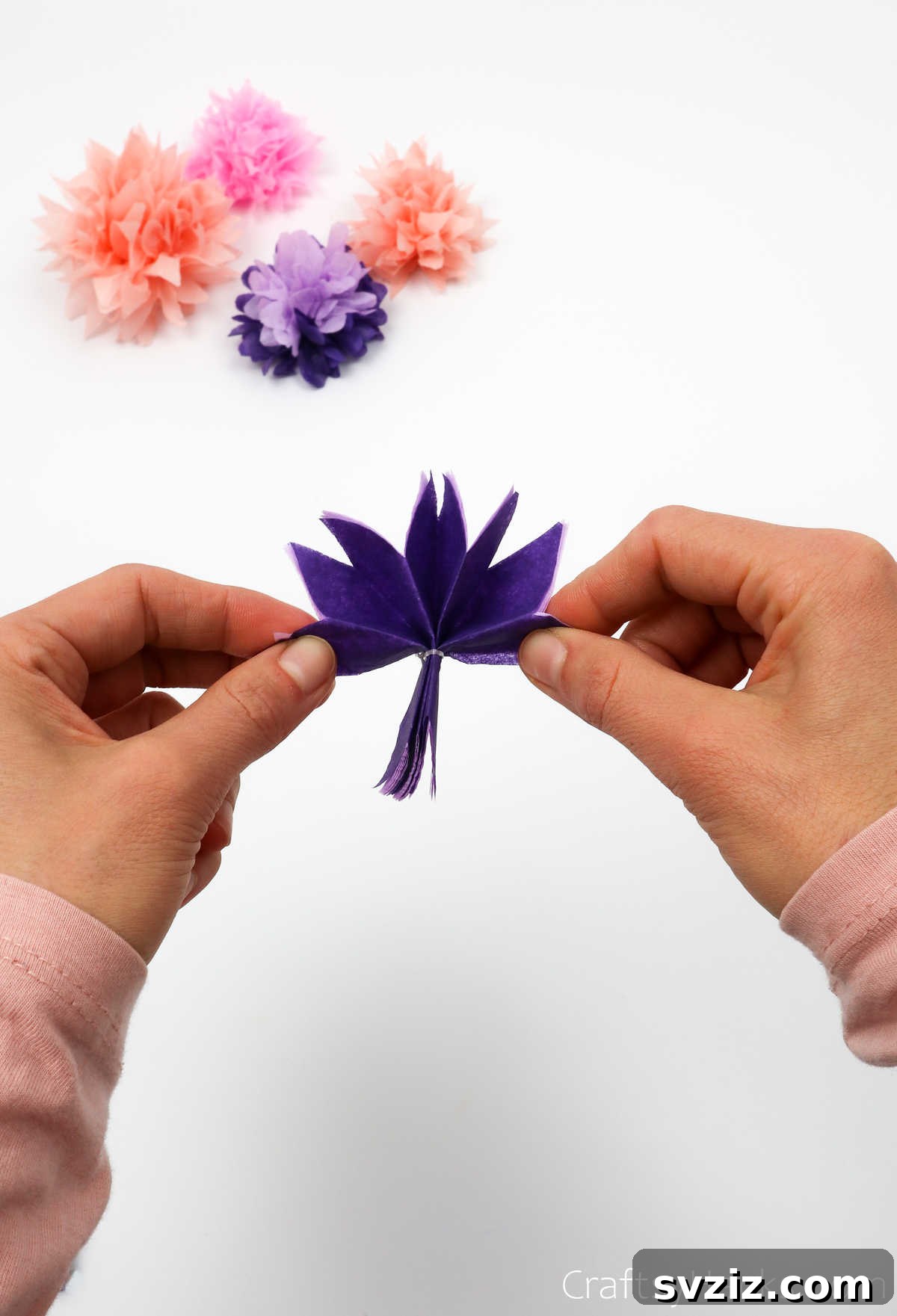 A hand gently separating and unfolding layers of tissue paper from a tied bundle to form flower petals