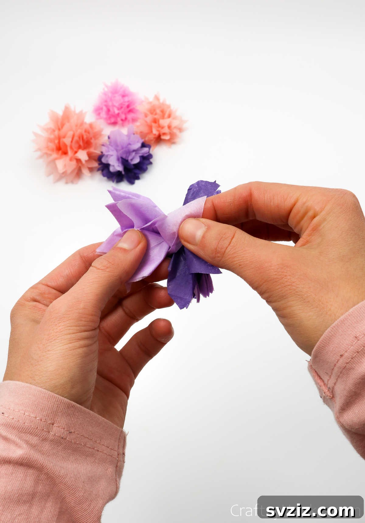 Close-up of hands delicately separating tissue paper layers to form the fluffy texture of a DIY flower