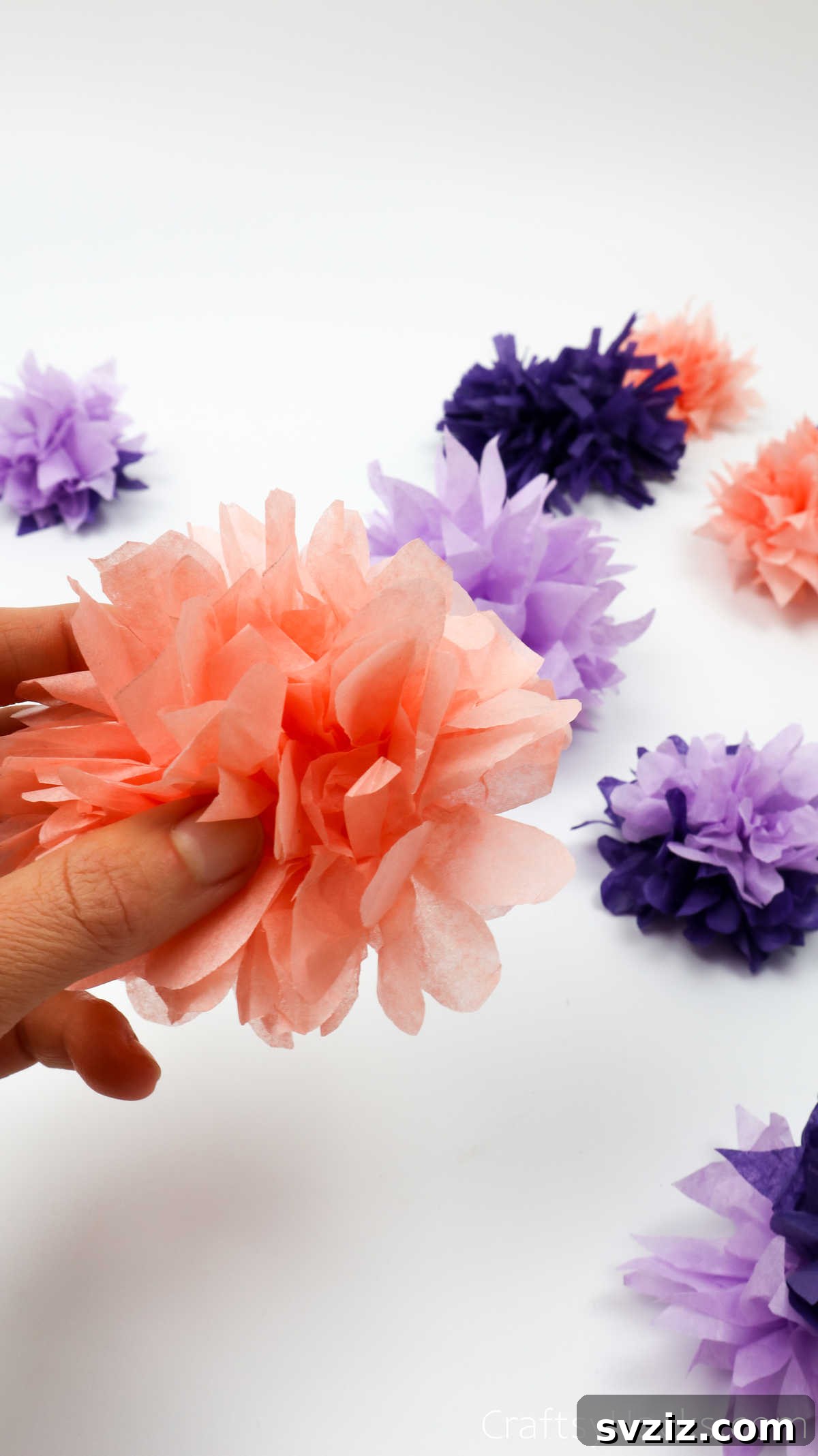 A hand holding a vibrant, fluffy tissue paper flower, highlighting its delicate beauty and handmade charm