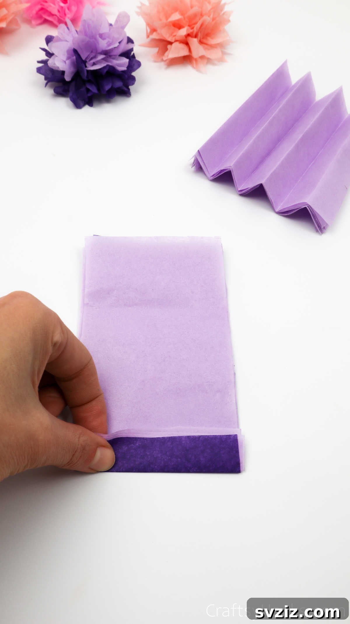 A person carefully folding a stack of tissue paper into an accordion shape, resembling a fan