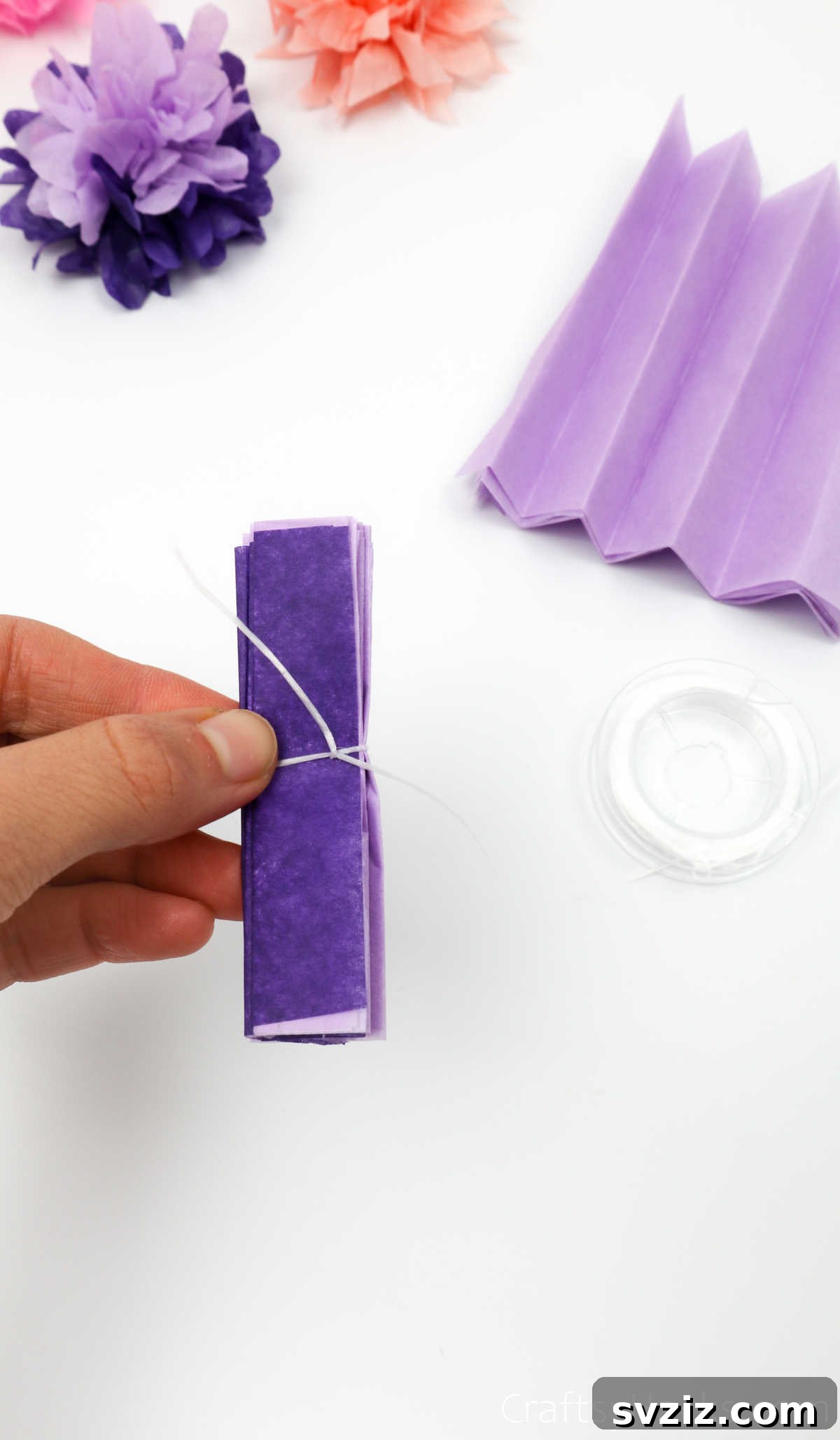 A folded tissue paper stack with a piece of thread tied securely around its midpoint, ready for shaping