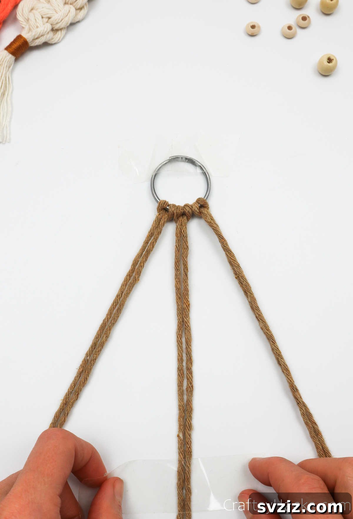 The two middle cords of the macrame keychain are taped down to the work surface.