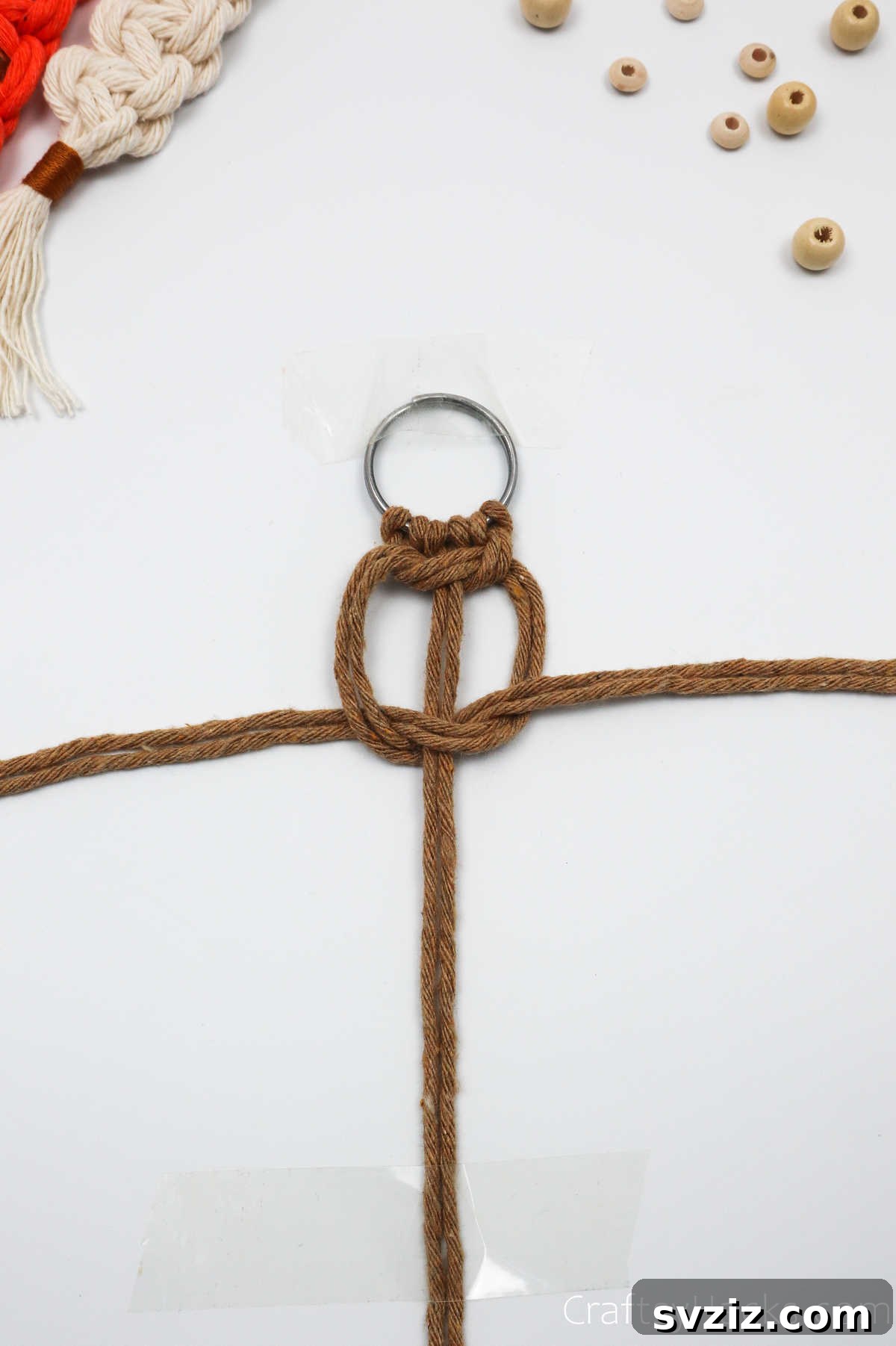 The second half of the square knot is tightened, completing the first full macrame square knot.