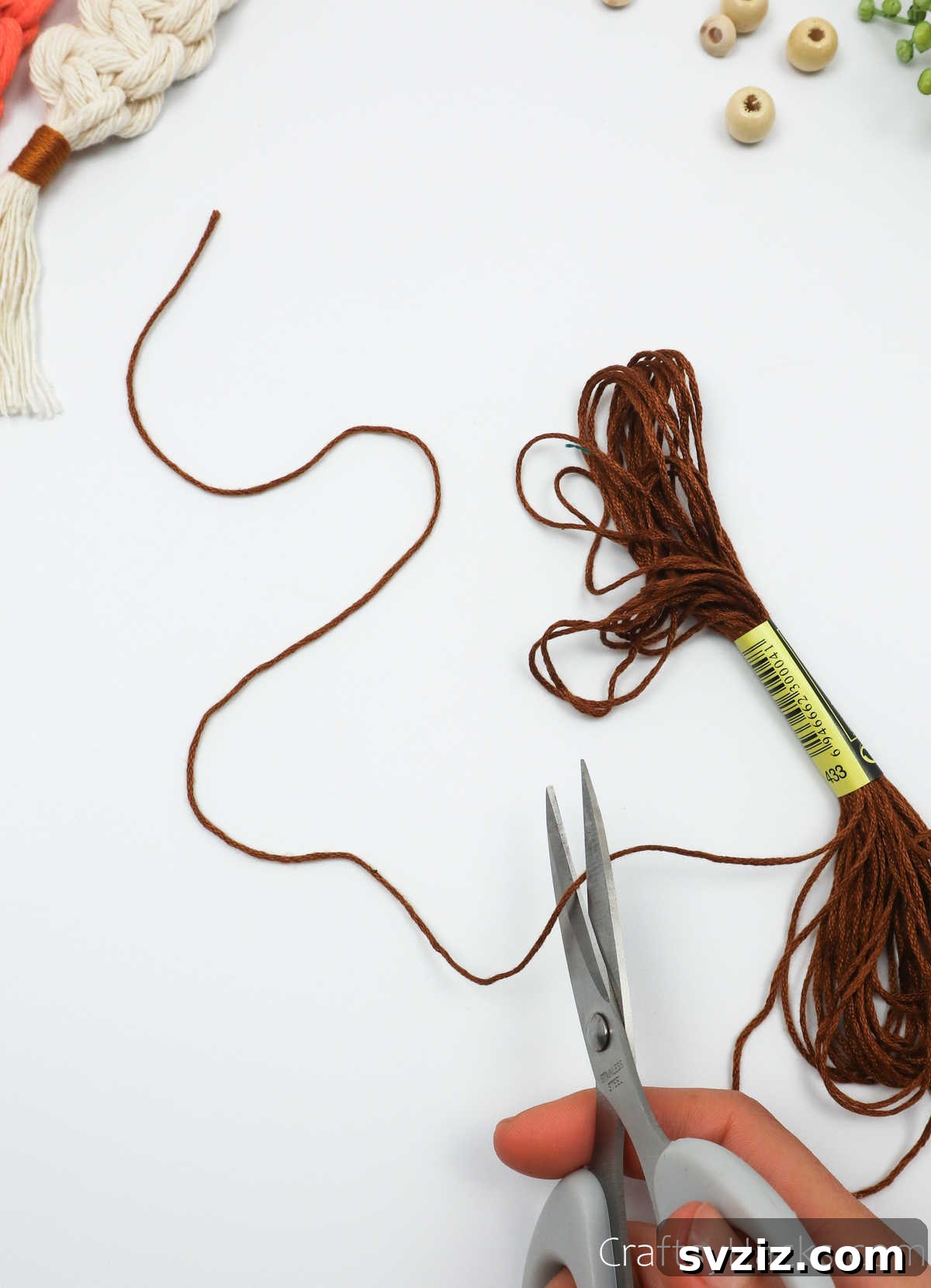 Cutting a length of brown embroidery thread for the finishing wrap of the macrame keychain.