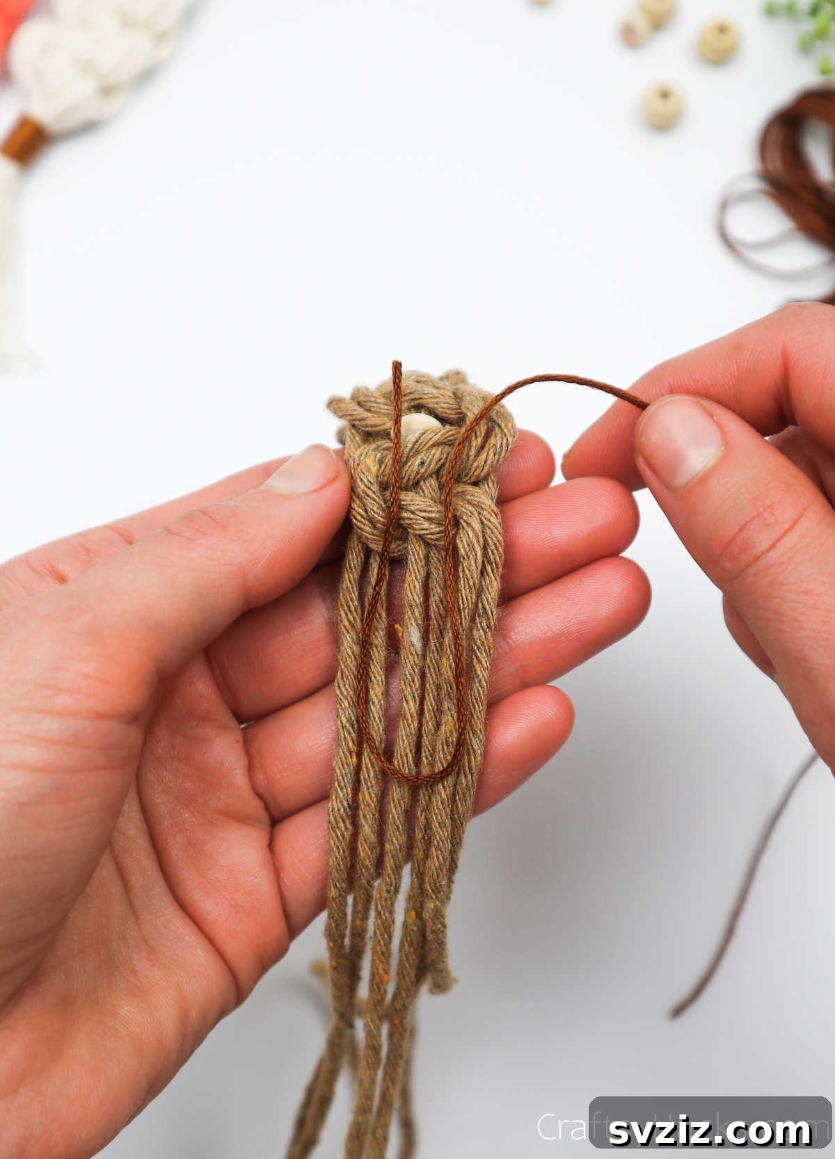 The embroidery thread is positioned to form a 'U' loop over the macrame cords, preparing for the finishing wrap.