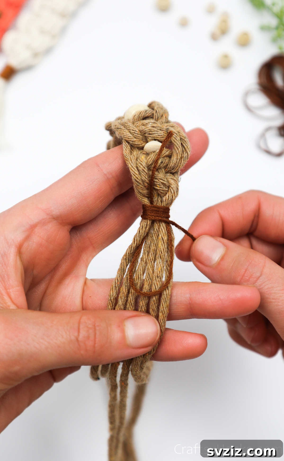 Wrapping embroidery thread around all macrame cords at the bottom of the knotted section.