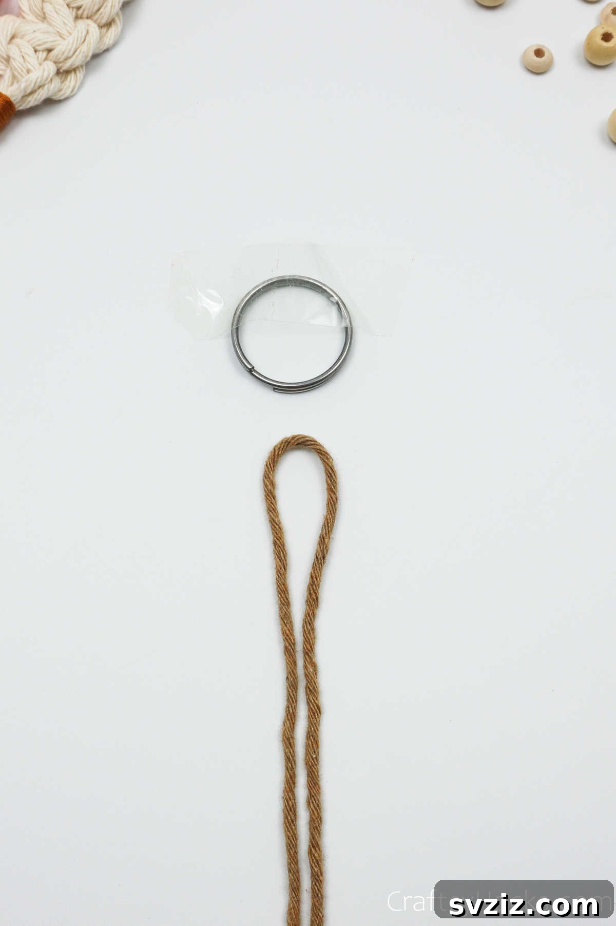 A macrame cord folded in half, ready to be attached to a key ring that is taped to a surface.