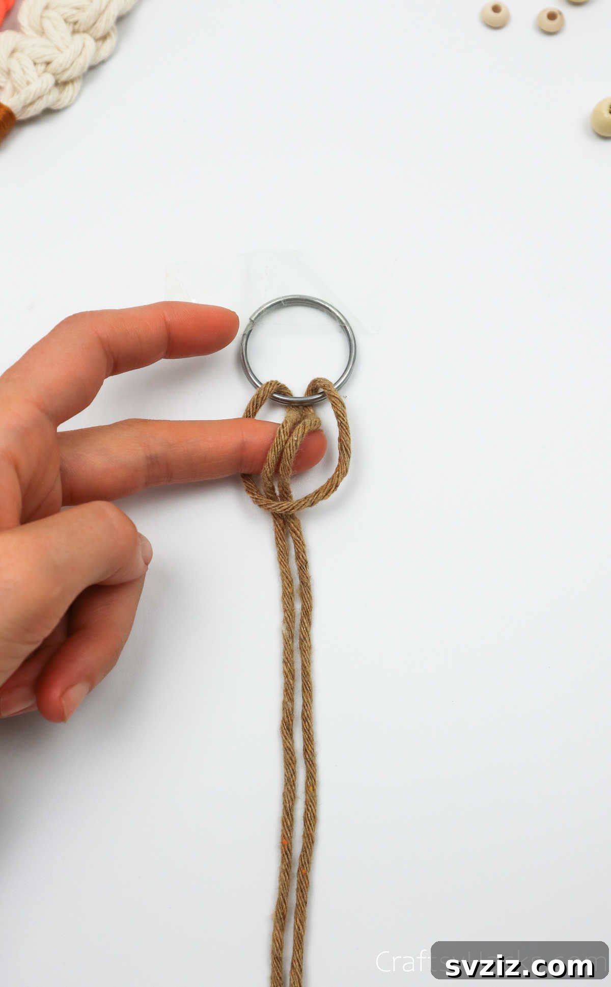 The two ends of the macrame cord are pulled through the loop to tighten the lark's head knot.