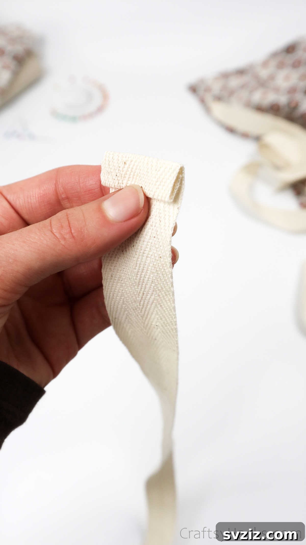 Craft Your Own Custom Apron 30 The process of rolling and securing the edge of a ribbon with a pin, ensuring a neat and finished look for the apron straps.