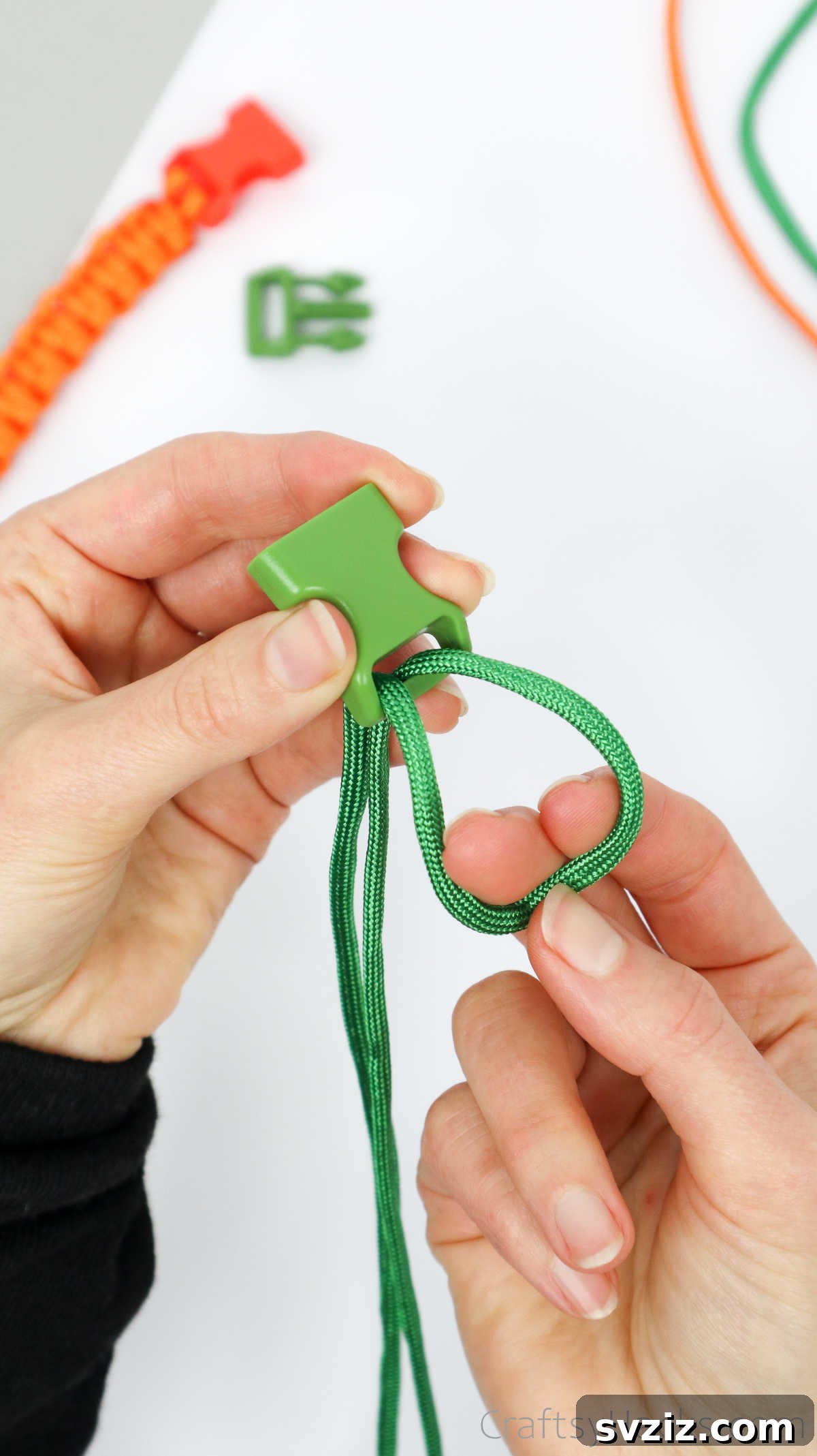 The paracord threaded through the buckle, forming a visible loop, with the two loose ends ready for the next step.
