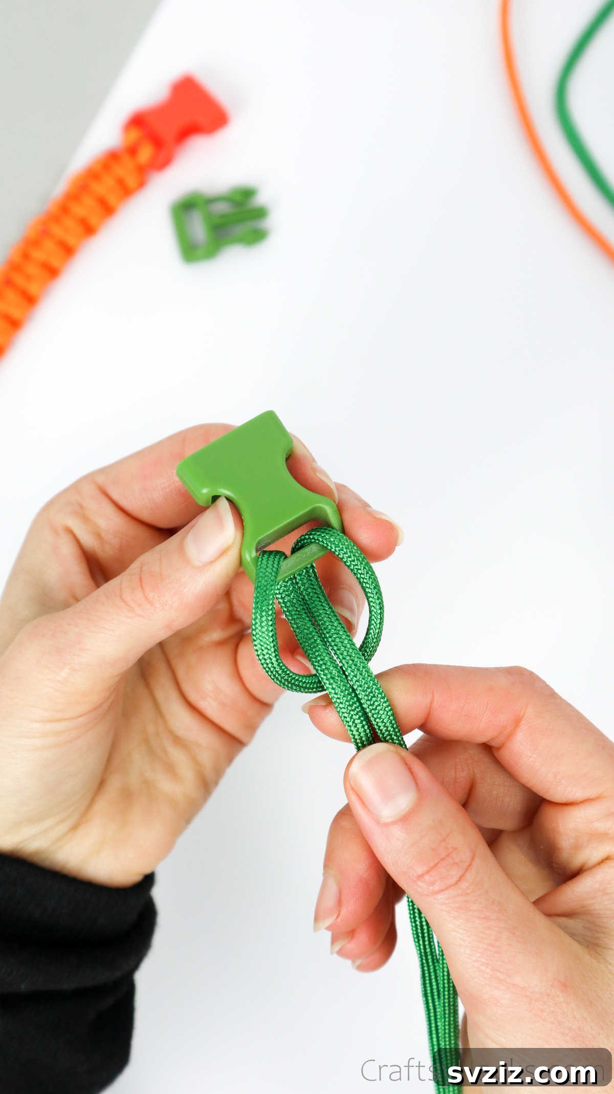 Both paracord ends being pulled to tighten the Lark's Head knot, securing it firmly to the buckle.