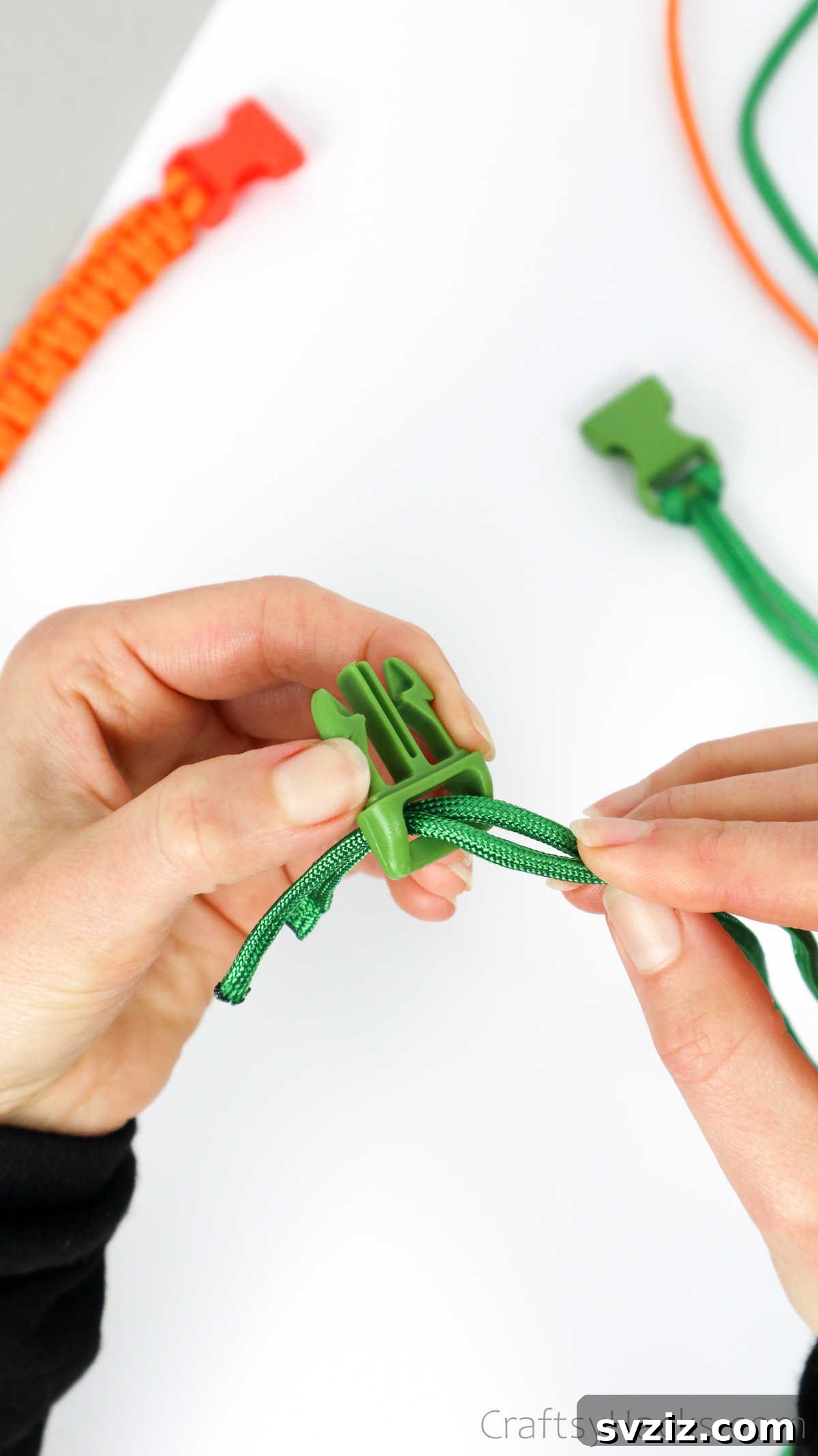 The two paracord strands being threaded through the slots of the second buckle half.