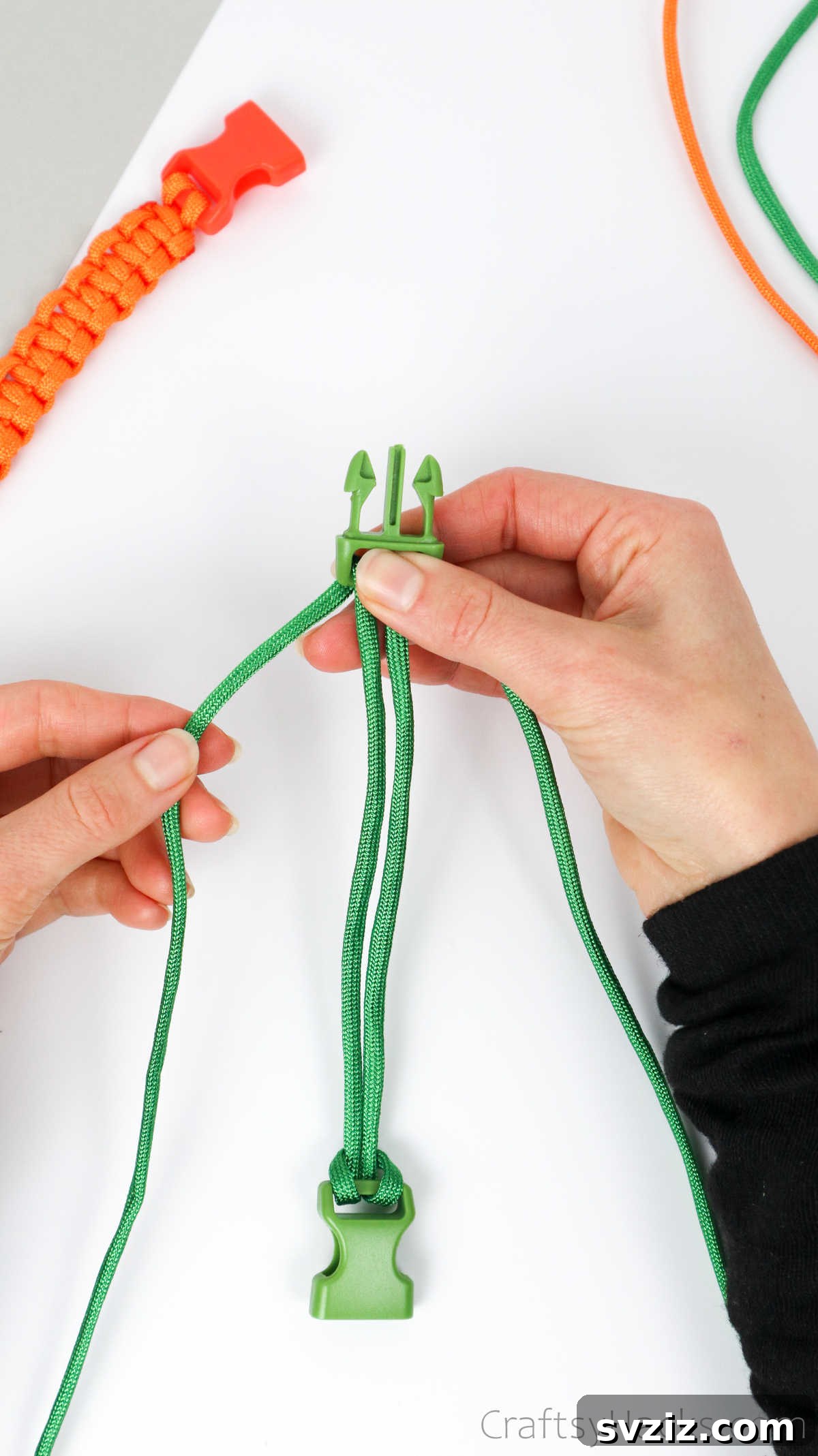A hand holding the paracord against the buckle, ready to begin the square knot weaving process.