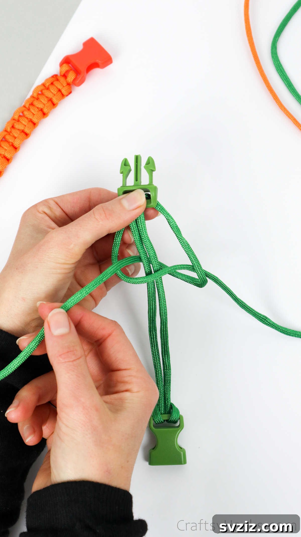The right paracord end being pulled up and through the left-side loop to tighten the initial knot structure.