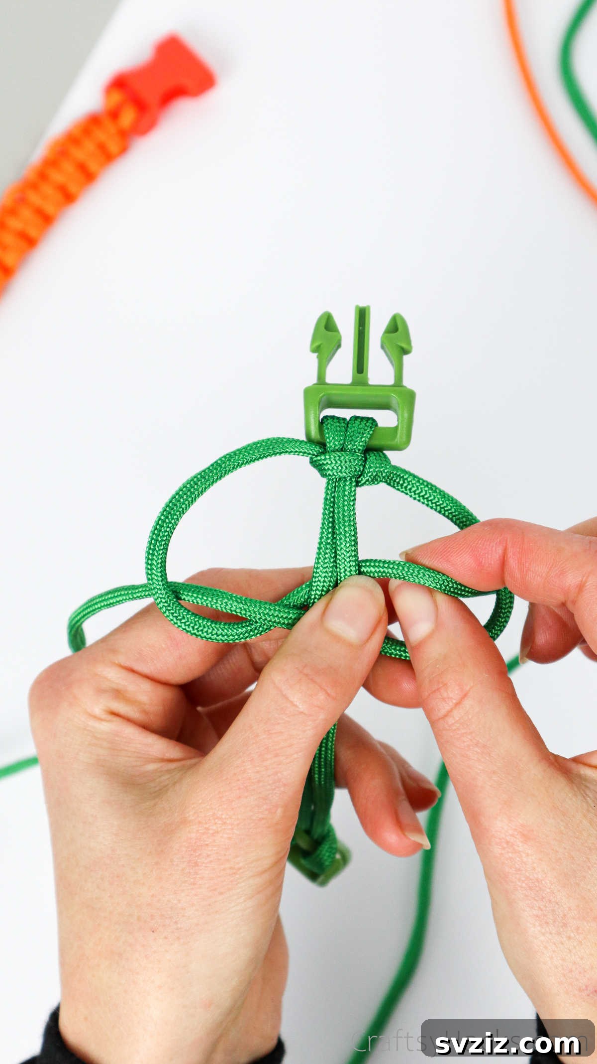 The left paracord end being pulled through the right-side loop, tightening the second half of the square knot.