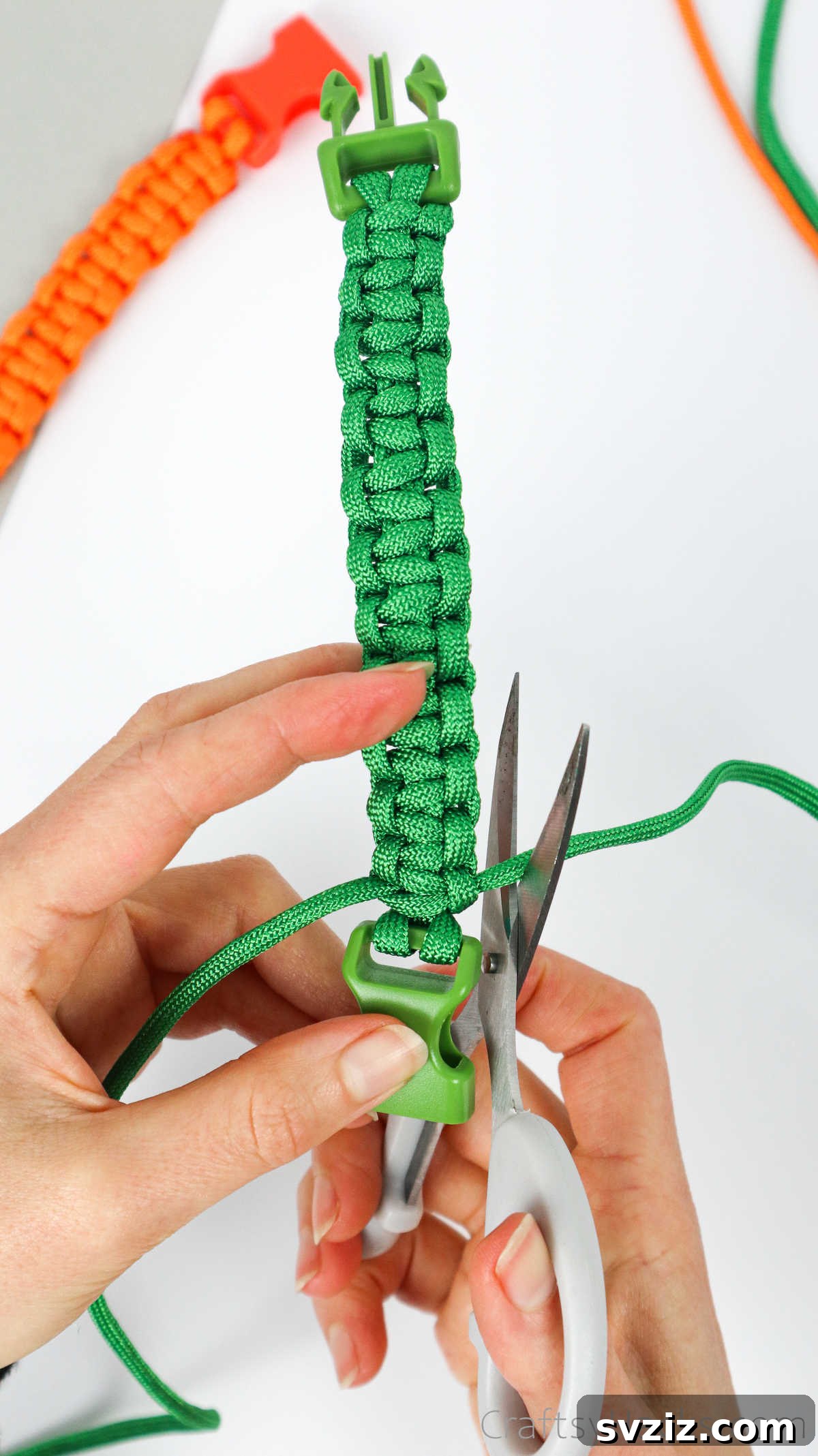 A hand using scissors to trim the excess paracord close to the last knot on the finished bracelet.