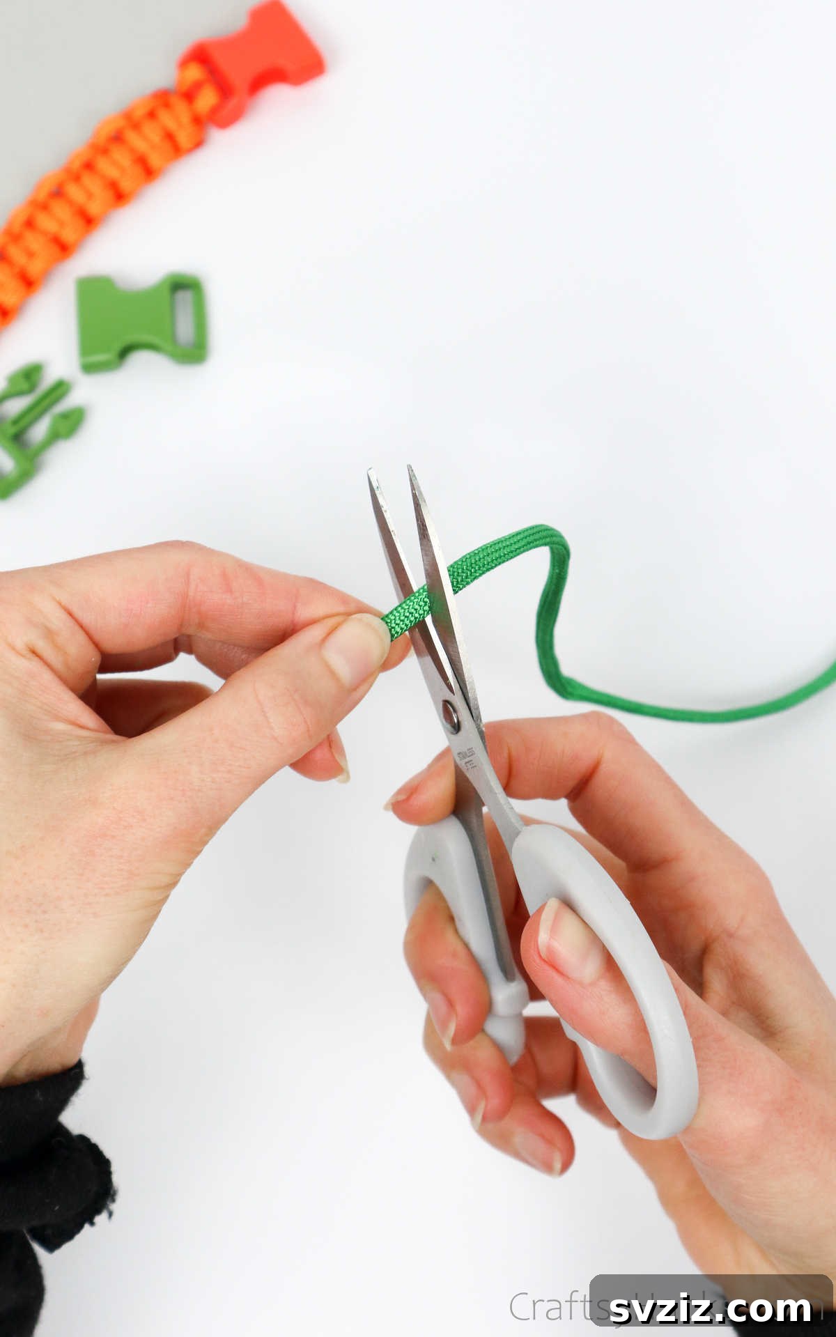 A close-up shot of hands using scissors to cut a length of paracord cleanly and precisely.