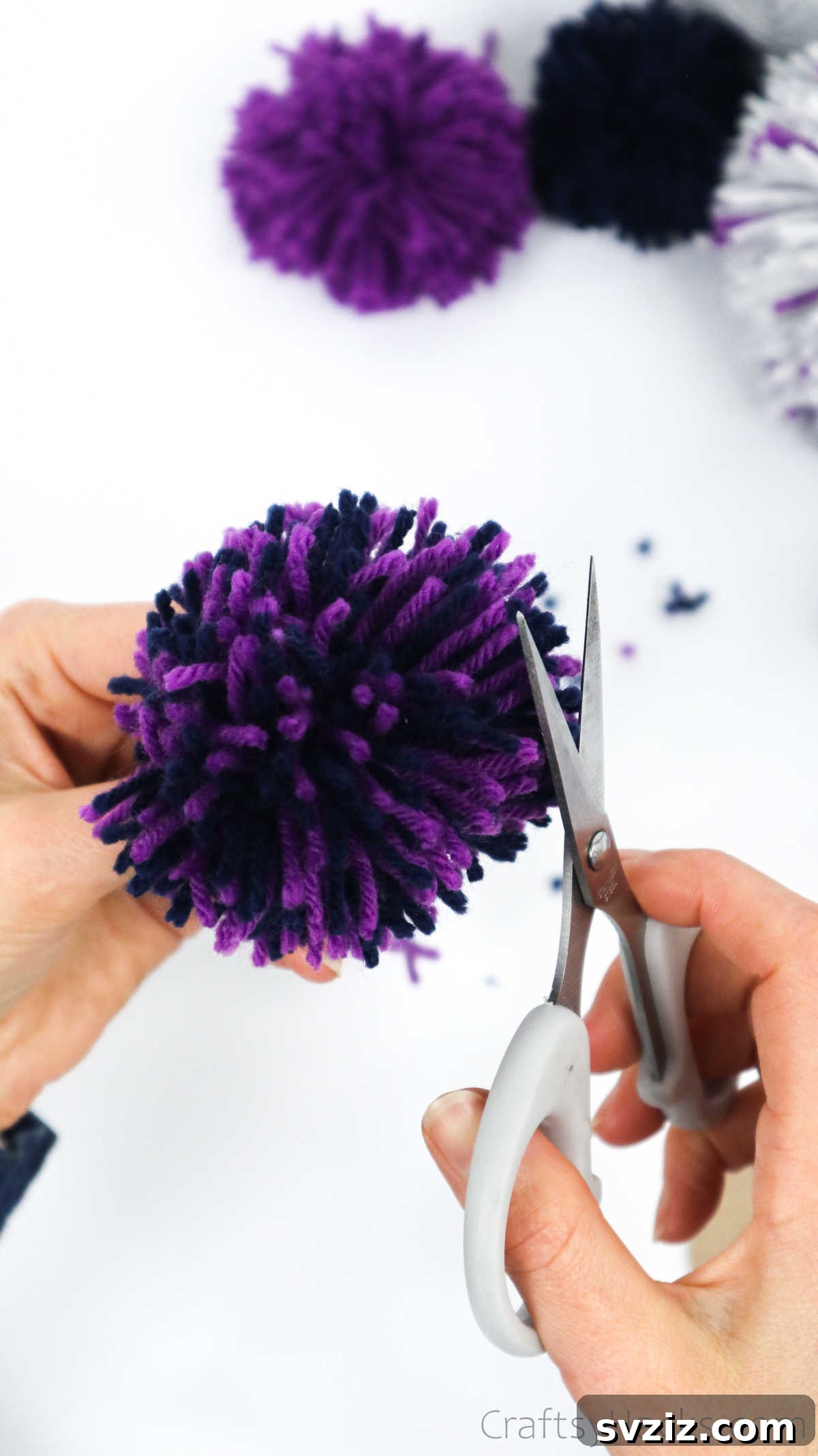 Trimming a yarn pom pom with scissors to achieve a perfectly round shape