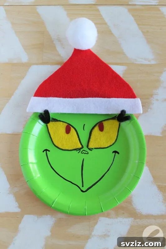Crafting Smiles: Paper Plate Fun for Kids 8 Paper plate Grinch craft featuring his iconic grumpy green face and a small Santa hat.