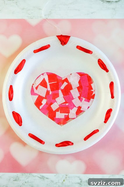 A vibrant heart-shaped sun catcher made from colorful tissue paper and a styrofoam plate, perfect for window decor.