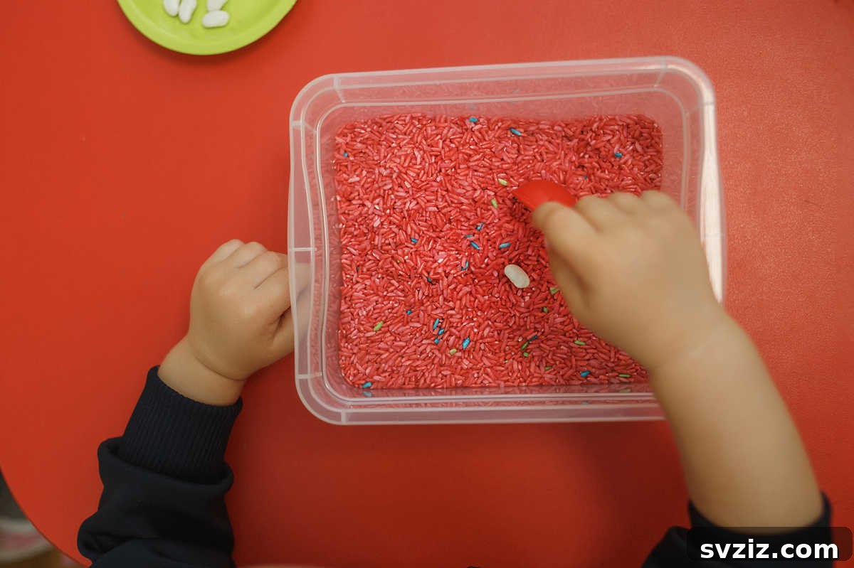 Toddler playing with a sensory bin filled with colorful pasta, excellent for 1-year-old development.