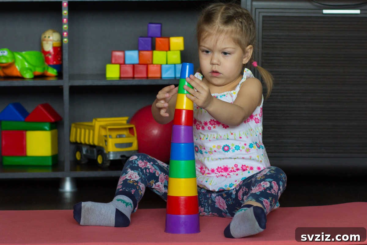 41 Creative Play Ideas for Two-Year-Olds 8 A toddler focused on carefully stacking colorful plastic cups.