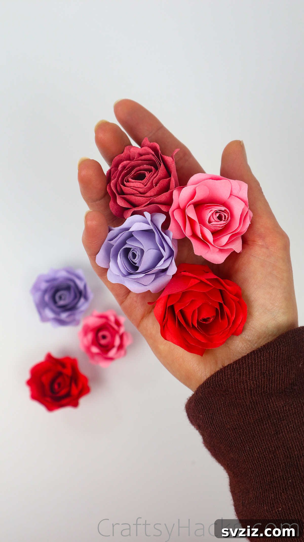 Your Simple Guide to Gorgeous Paper Roses 4 A hand gently holds a collection of finished DIY paper roses, showcasing their intricate details