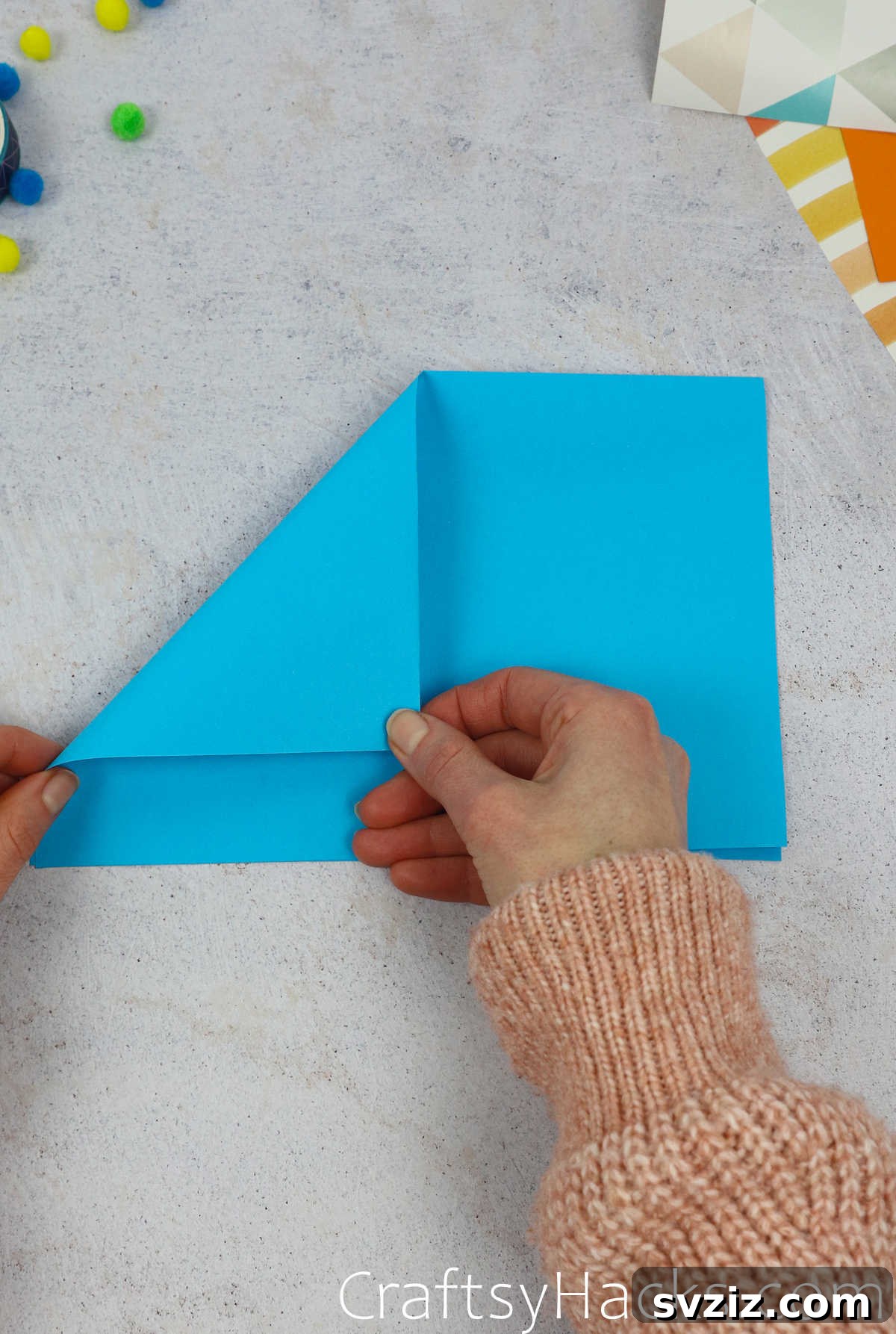Folding the top left corner of the blue paper down to the center crease to form one side of the hat's peak.