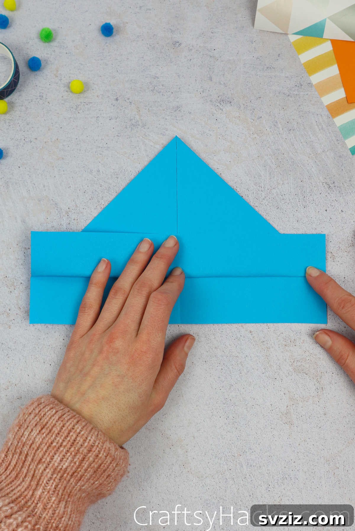 The bottom edge of the paper is folded upwards, covering the base of the triangles formed in the previous step.