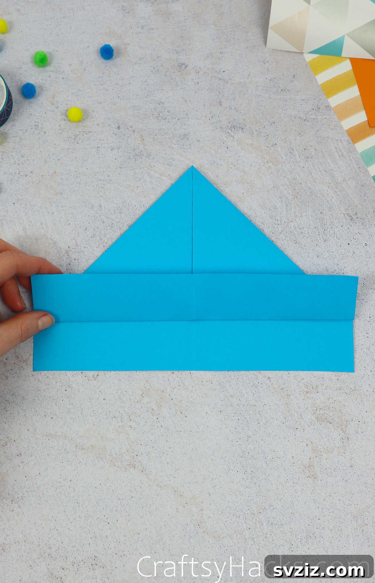The top layer of the bottom paper edge unfolded slightly to show the crease and preparation for the next fold.