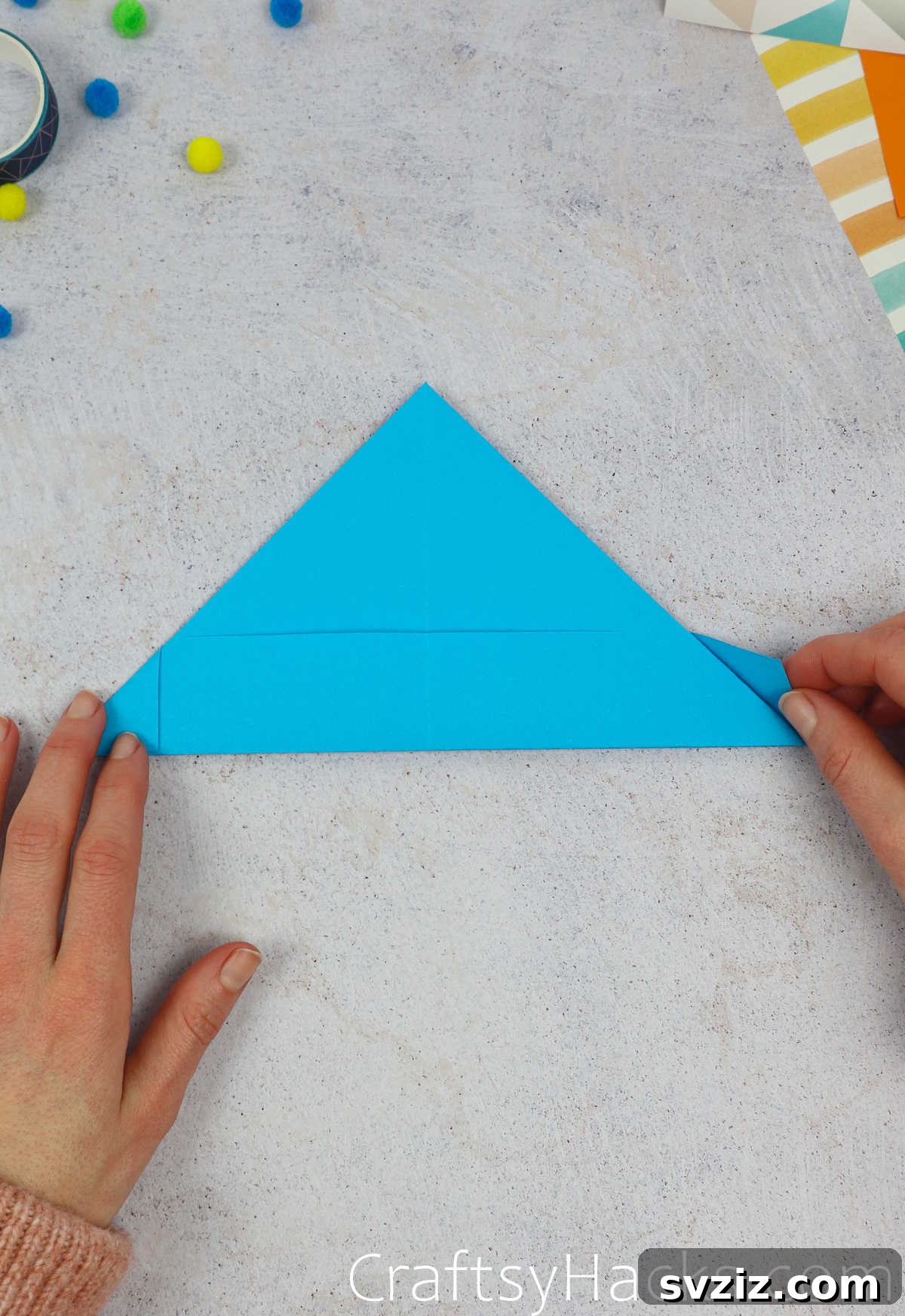 A hand gently folding in an edge of the paper hat, preparing it for reinforcement.
