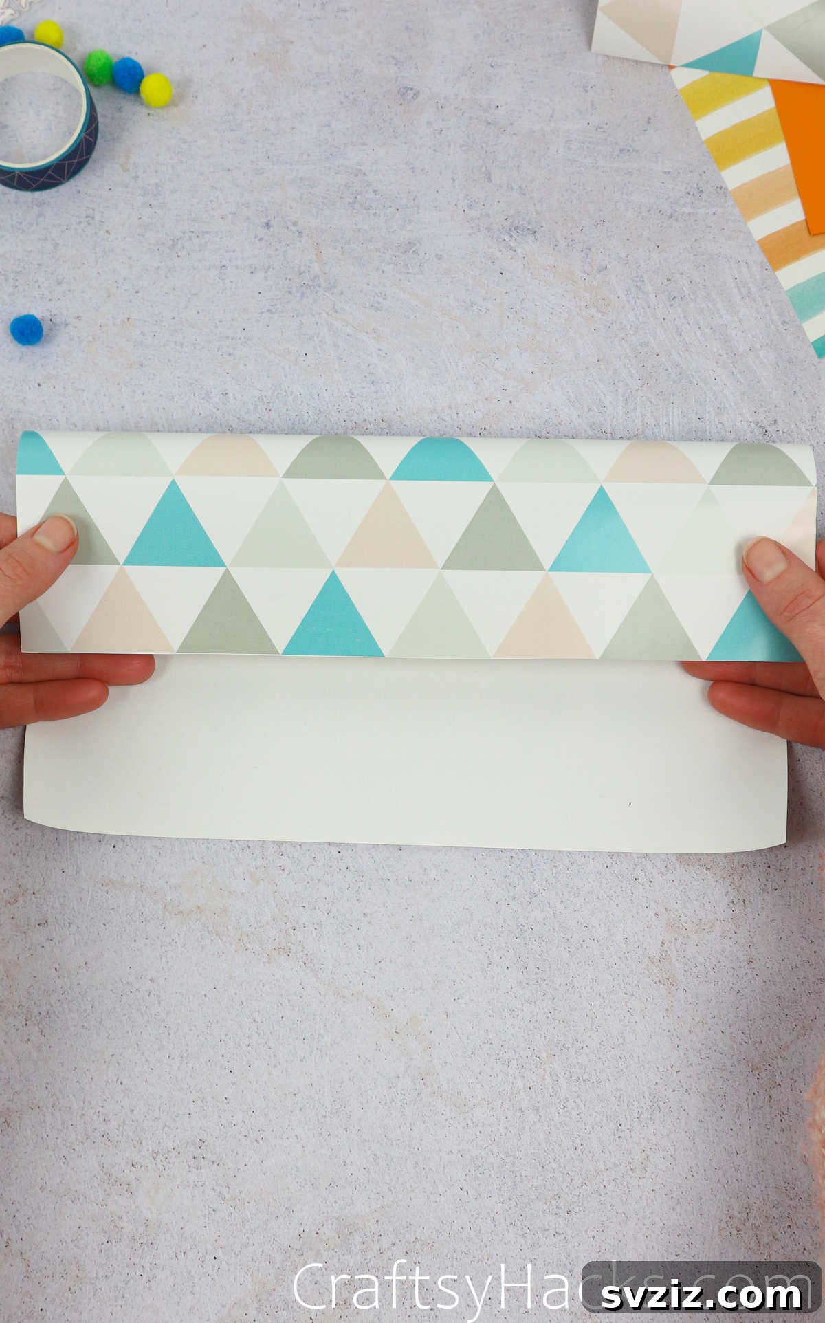 A hand demonstrating the final fold, ensuring the colored side of the paper is facing outwards.