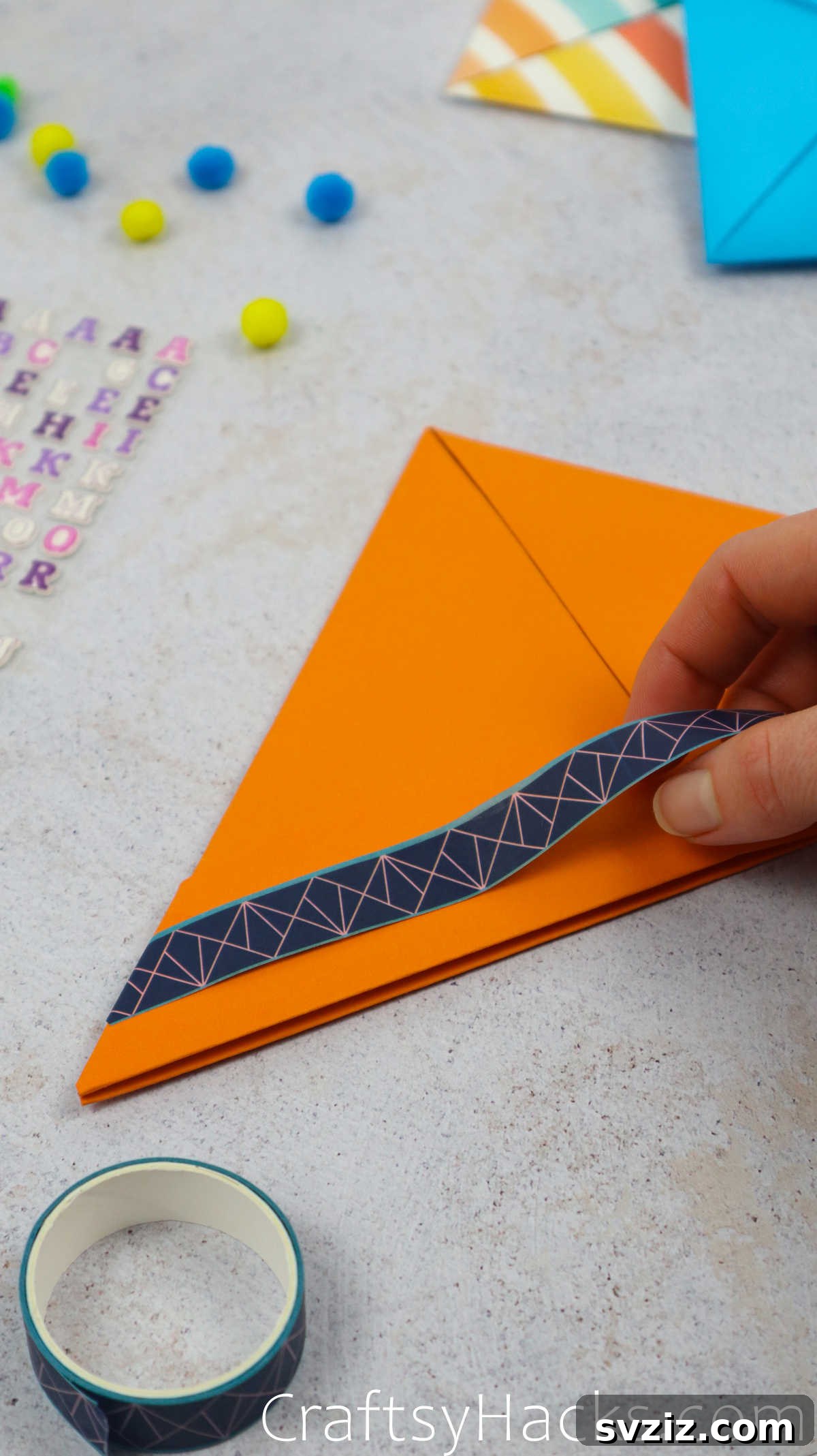 A hand applying decorative washi tape along the brim of a paper hat for added visual appeal.