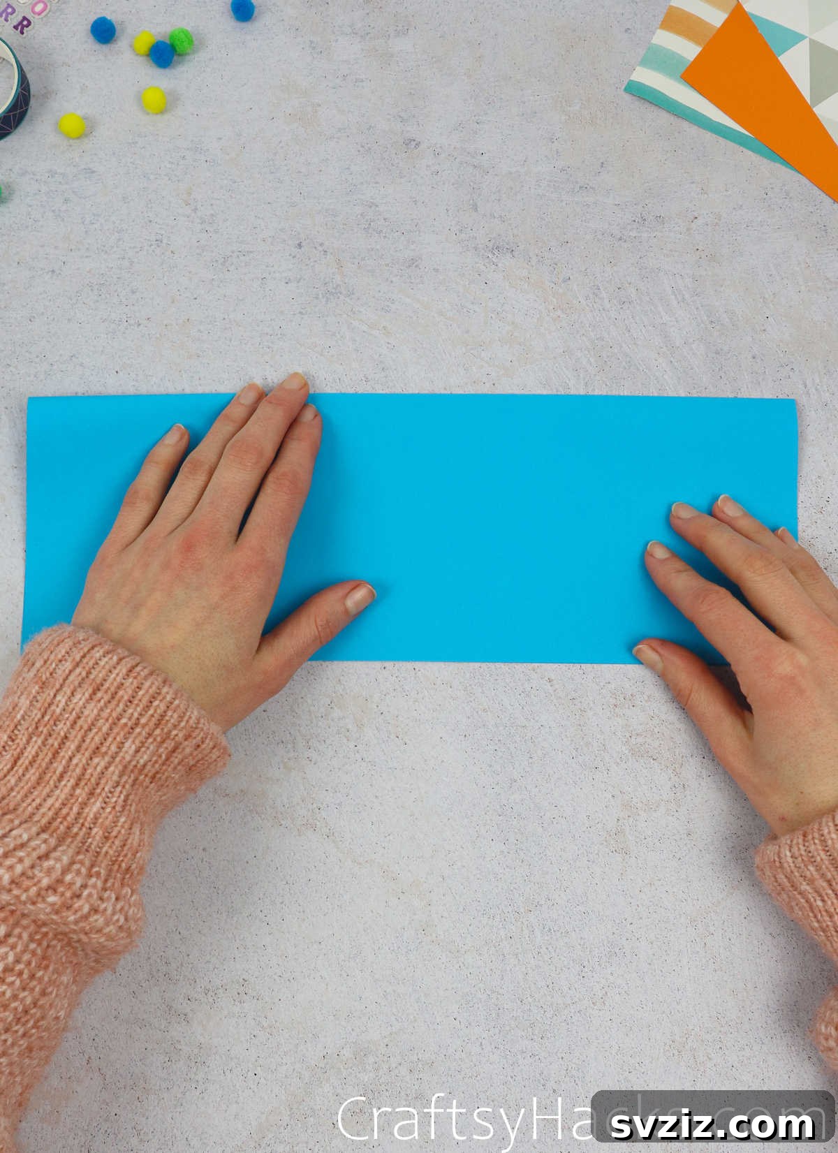 Close-up of a blue paper being folded, showing the precise alignment of edges for the initial fold.