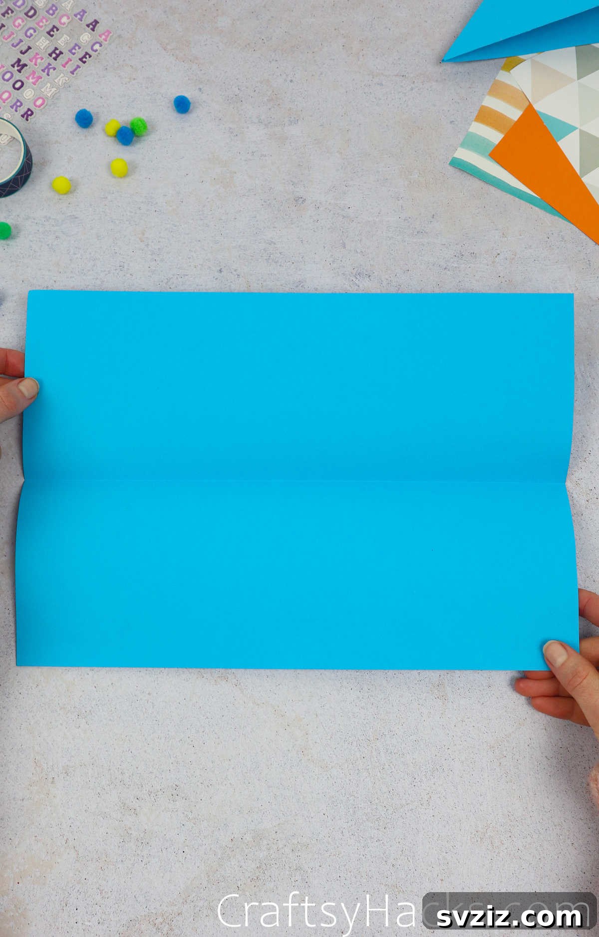 A partially unfolded blue paper, showing the existing crease and preparing for the next fold.
