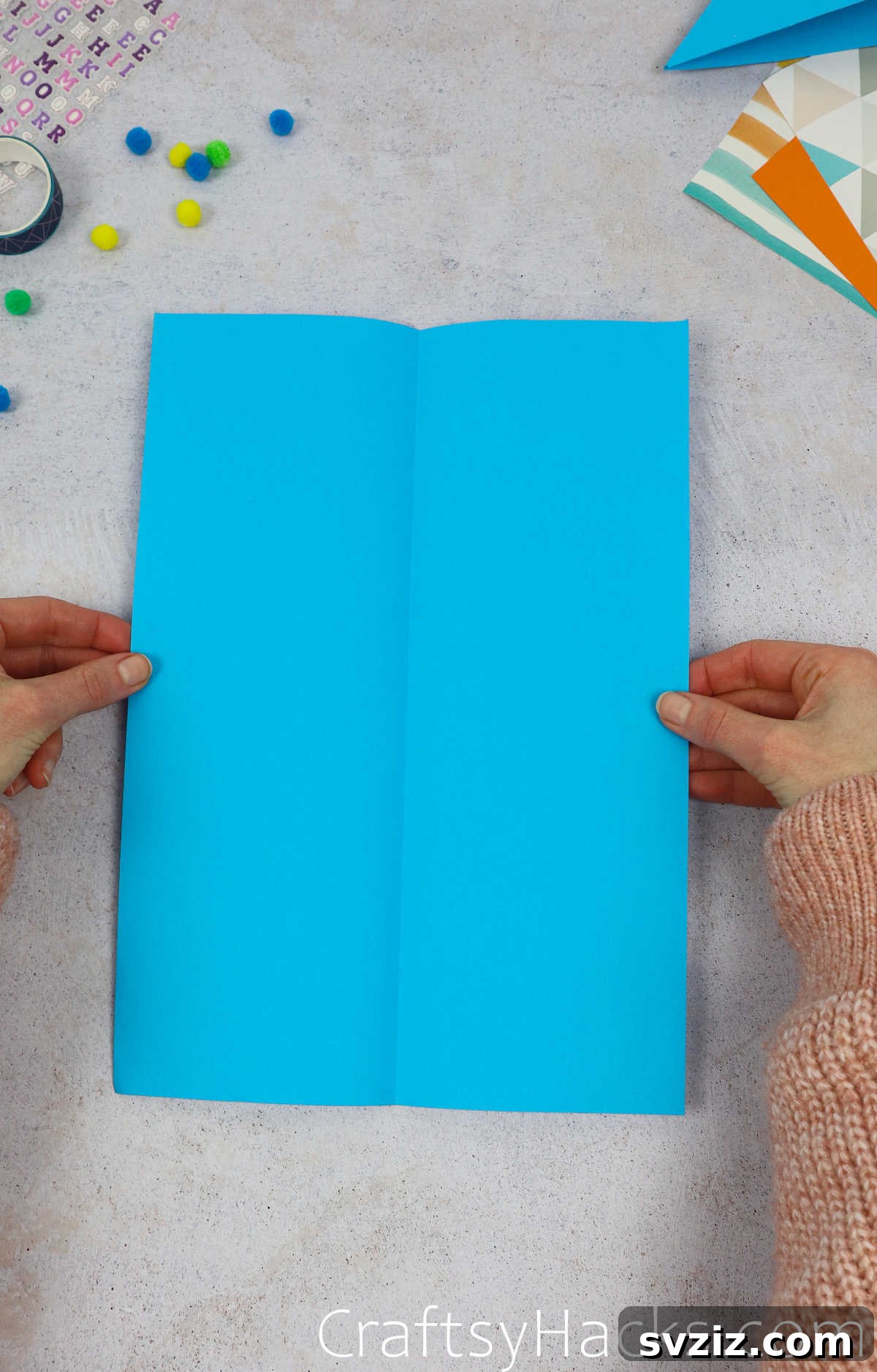The blue paper unfolded to reveal a central crease, ready for the next step of folding the corners.