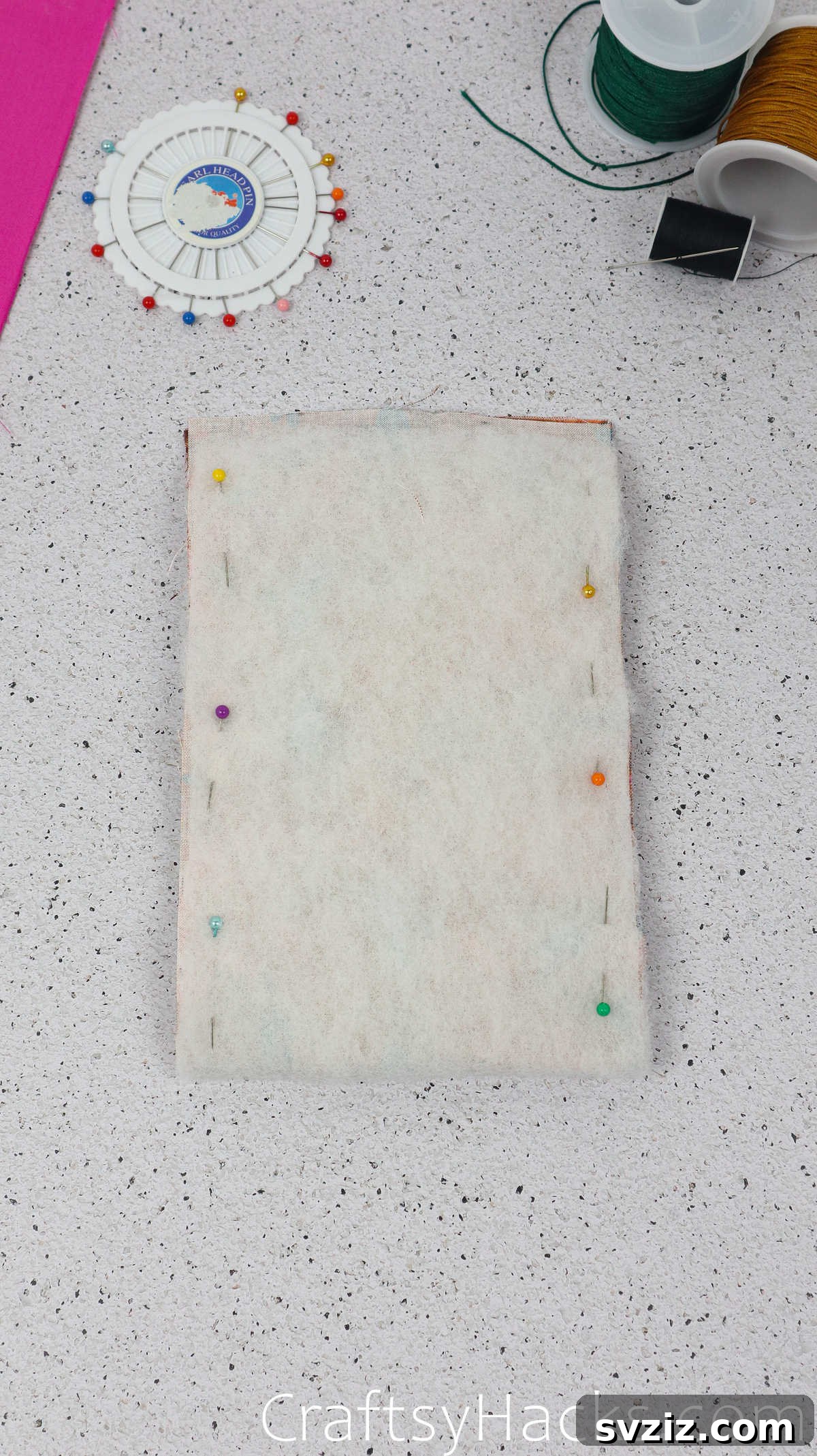 Pins securing the folded edges of the fabric and wadding, preparing the layers for stitching to form the pouch.