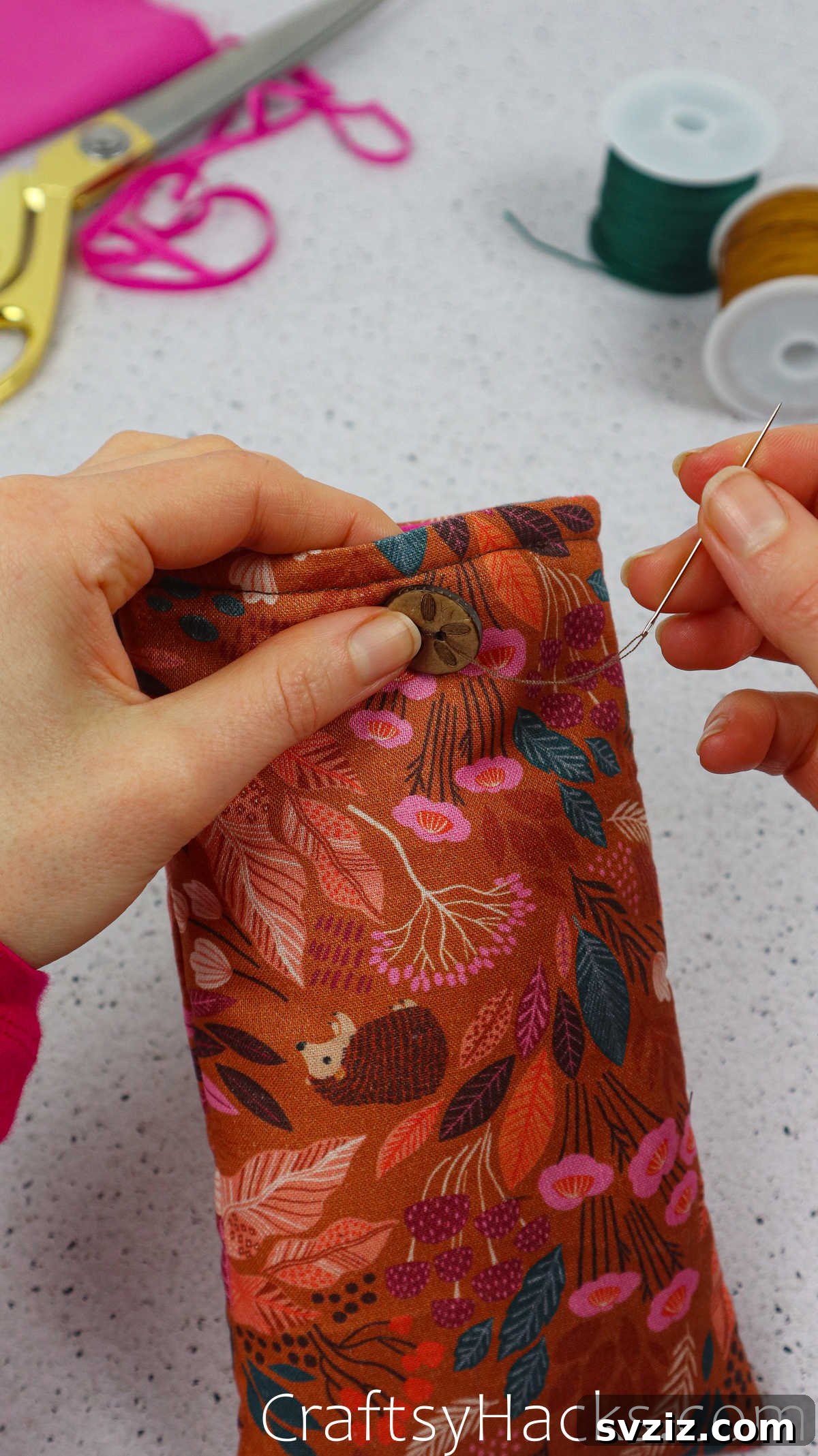 Hands sewing a decorative button onto the front of the fabric phone case, adding a functional and aesthetic element.