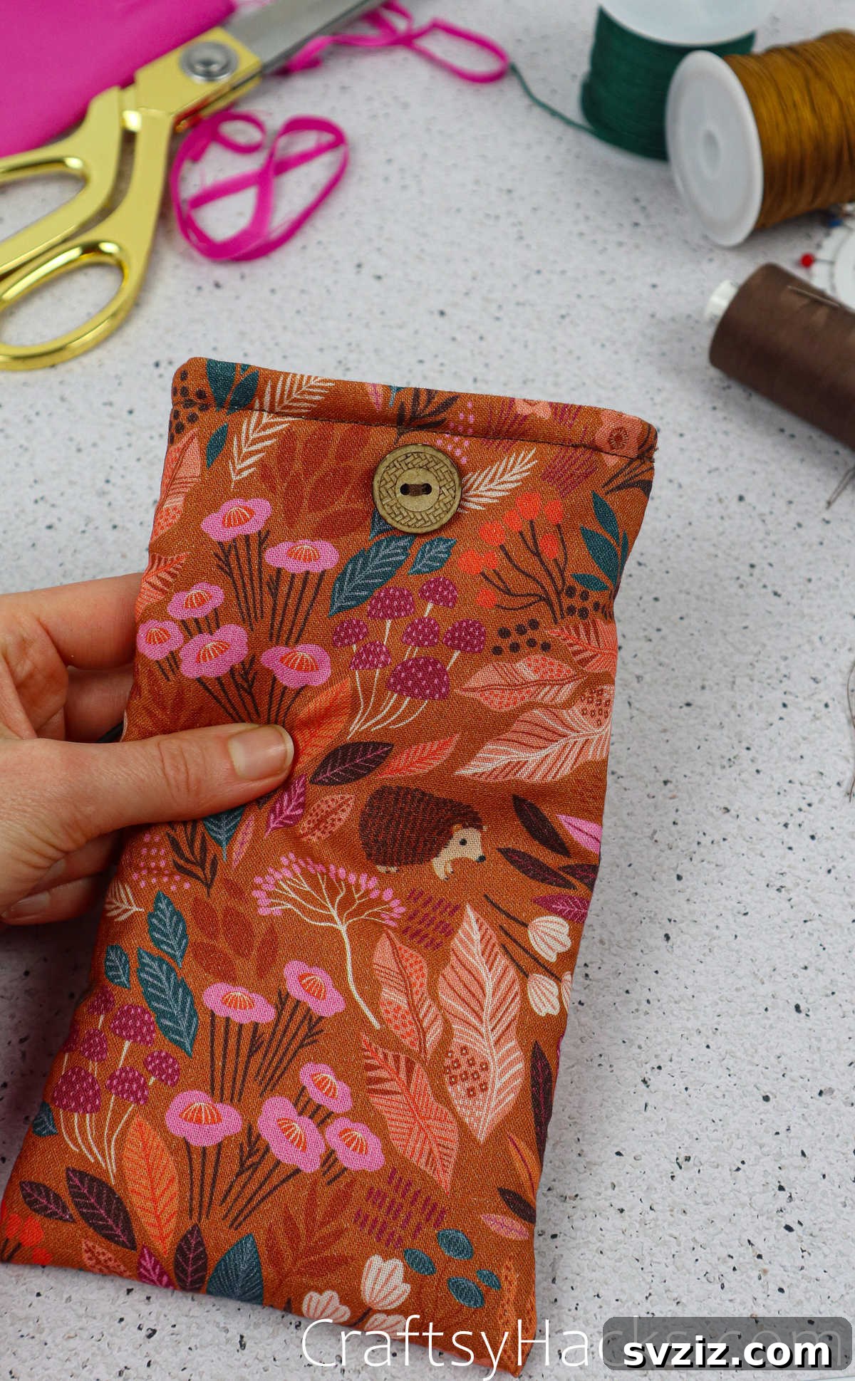 A securely sewn button on the fabric phone case, positioned for the elastic closure.