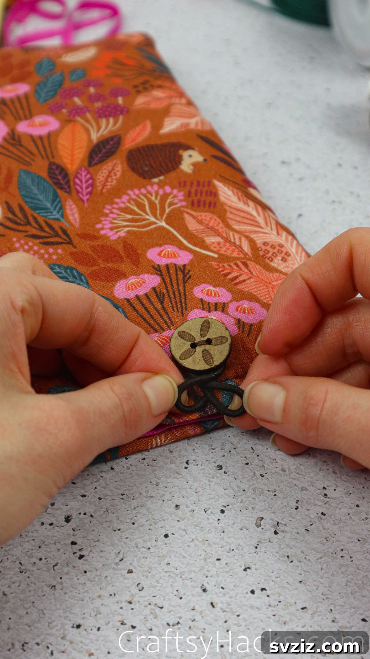 Hands carefully tying the elastic hair tie around the button, ensuring it is tight and secure.
