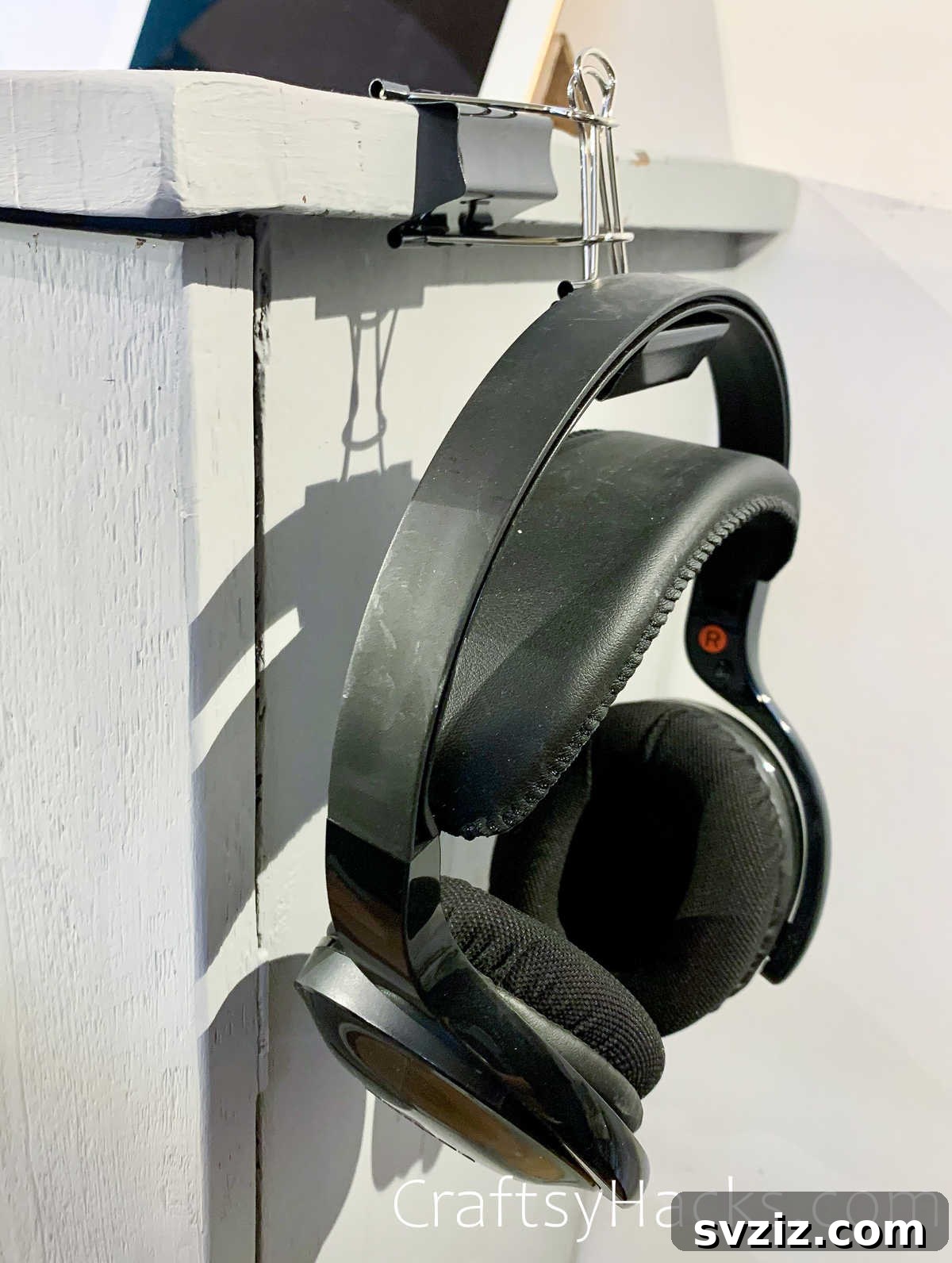Headphones neatly hung on a desk using two interconnected binder clips