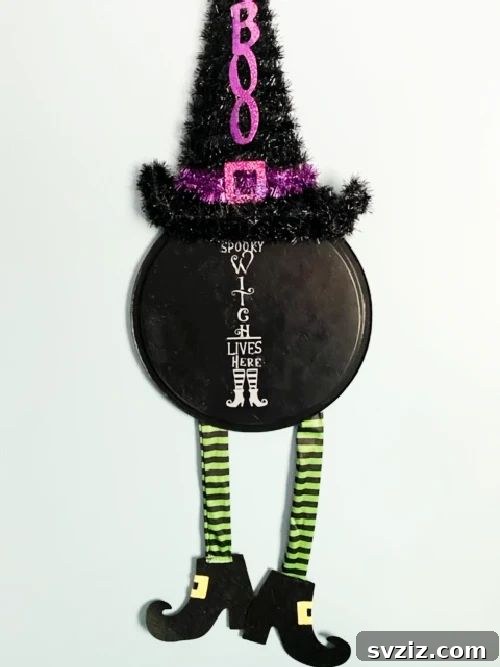 Charming and Eerie Witch Craft Projects 4 A quirky witch door hanger made from a pizza pan, featuring witch's legs and a hat.