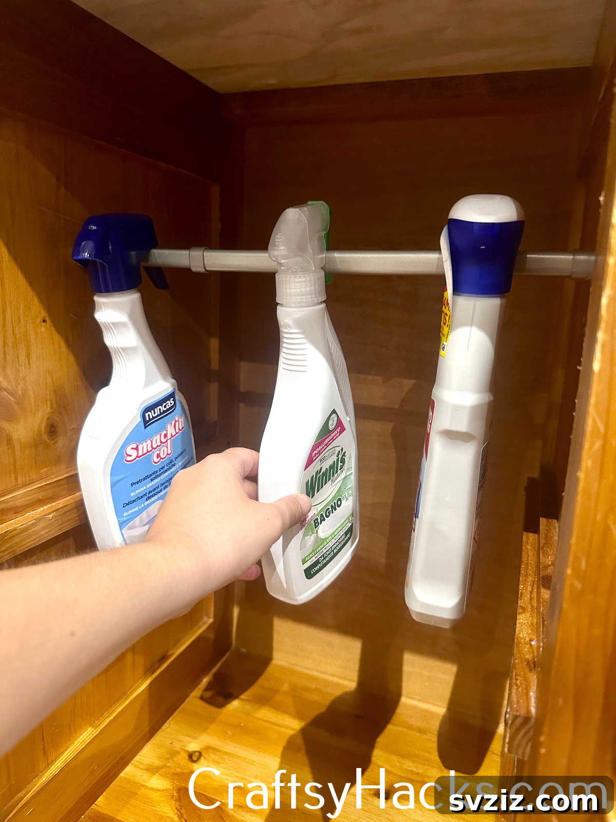 Hang cleaning spray bottles from a tension rod installed under a sink to save space and organize cleaning supplies.