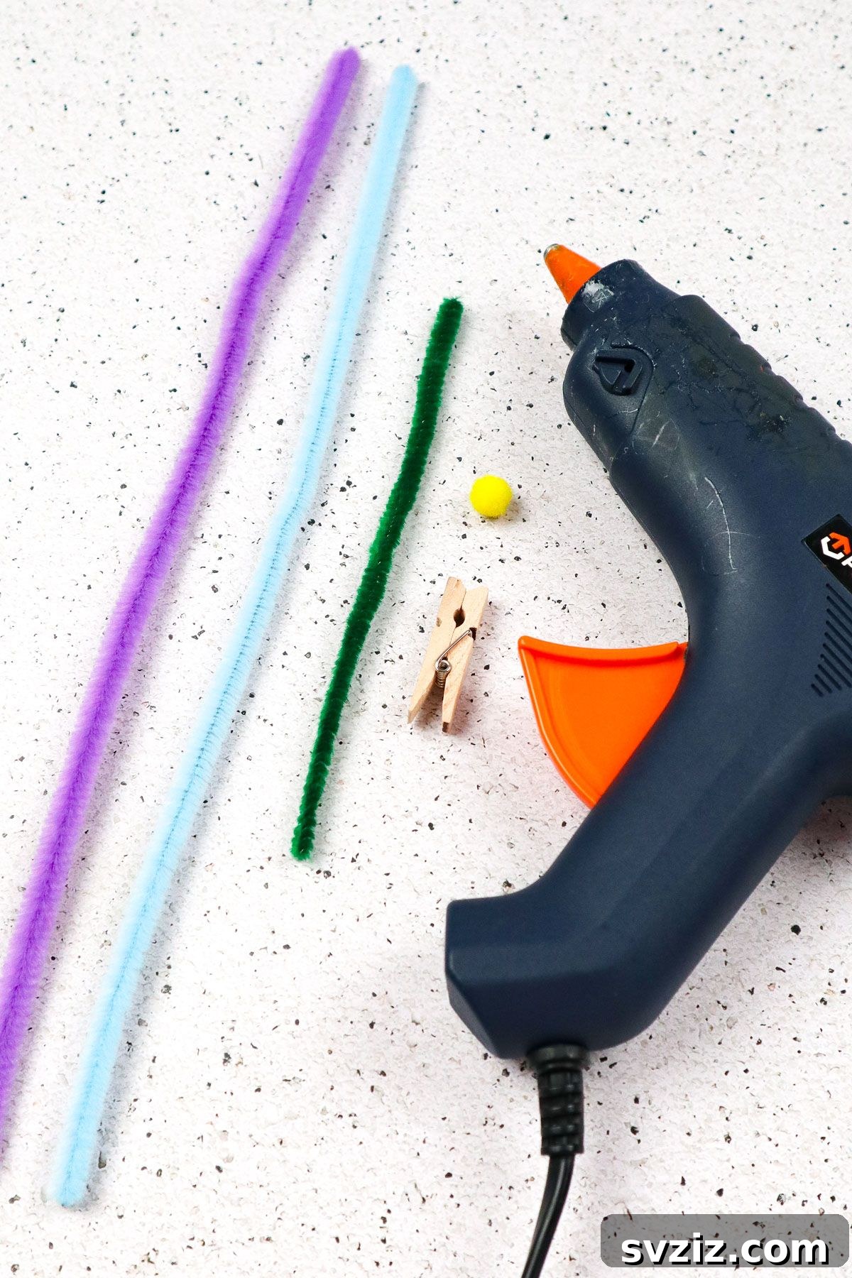 Assortment of craft supplies laid out, including colorful pipe cleaners, a hot glue gun, clothespin, and pom-pom, ready for making pipe cleaner butterflies.