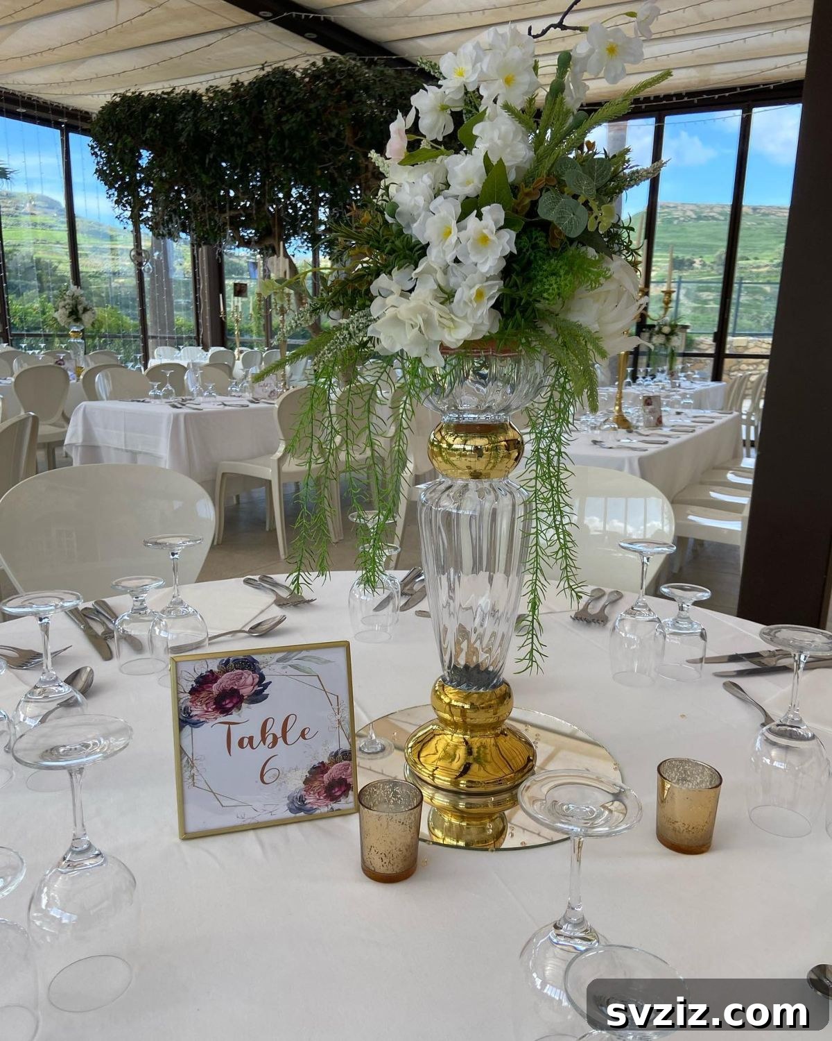27 Elegant Round Table Wedding Centerpiece Inspirations 5 Opulent tall glass vase centerpiece adorned with gold accents and vibrant flowers.