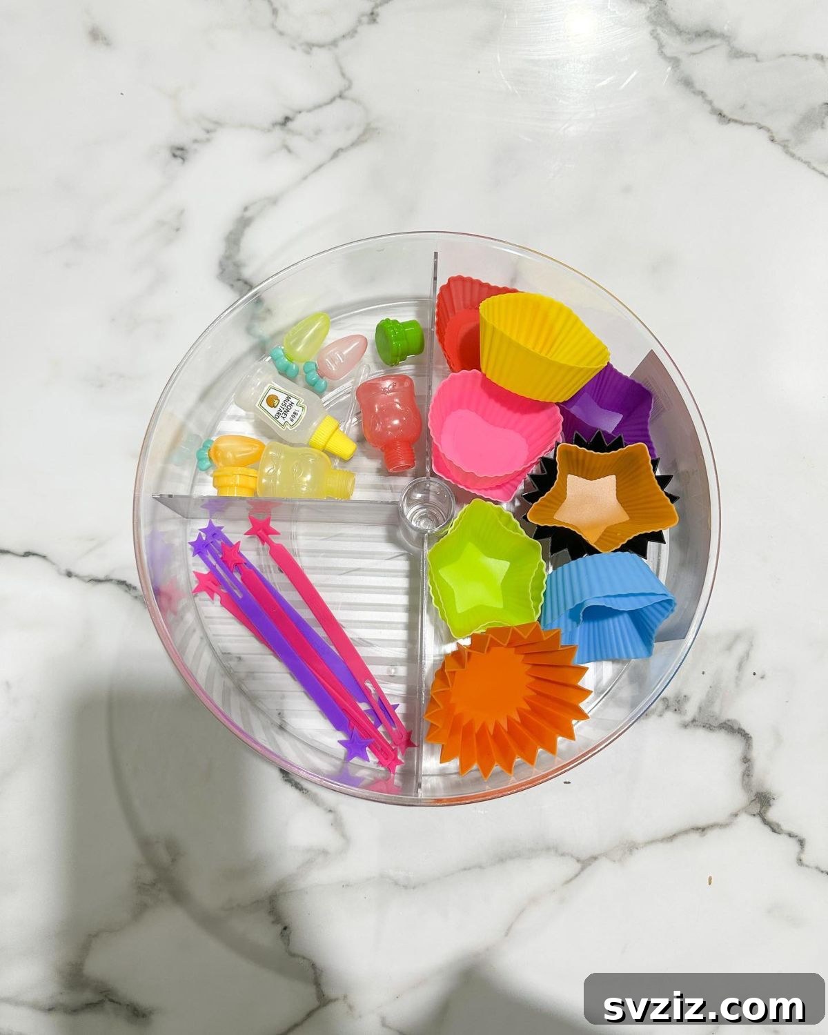 An acrylic turntable organizer with sections, holding various bento box accessories like silicone cups and picks.