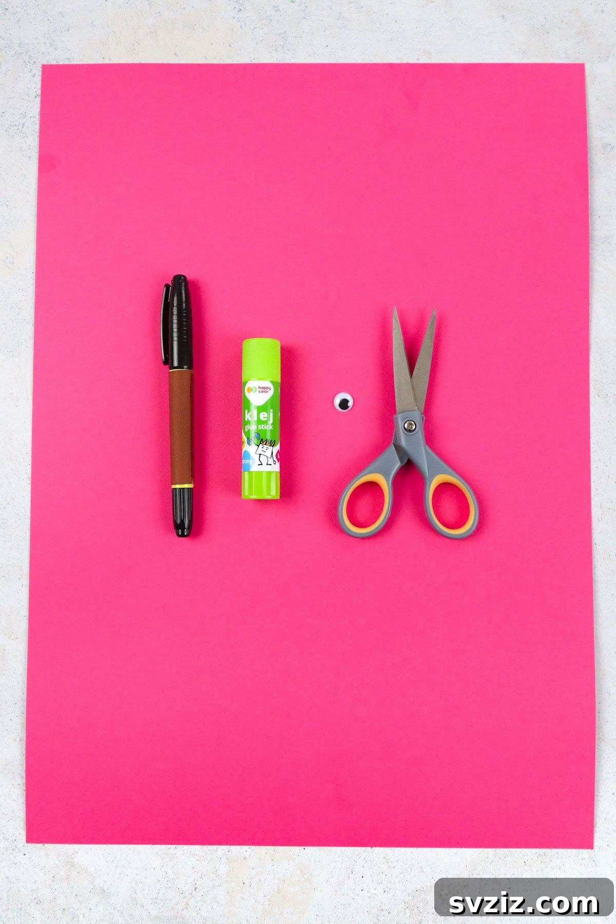 Flamingo Handprint Delight 3 Neatly arranged craft supplies including pink construction paper, scissors, googly eye, glue stick, and black marker on a wooden surface.